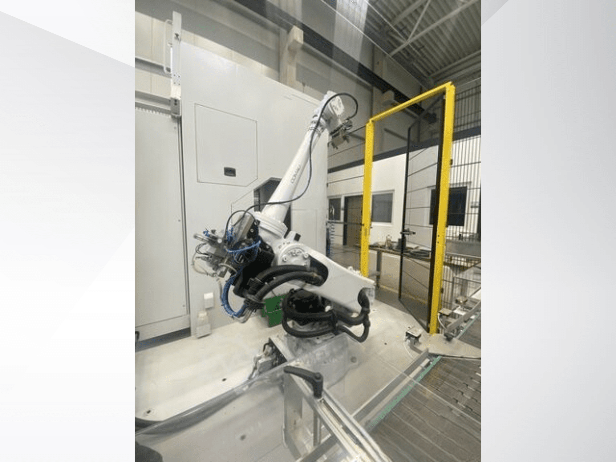 Robotické rameno COMAU Smart NJ 40-2.5 v bočním pohledu, s kabely a žlutou bezpečnostní bránou v továrním prostředí.