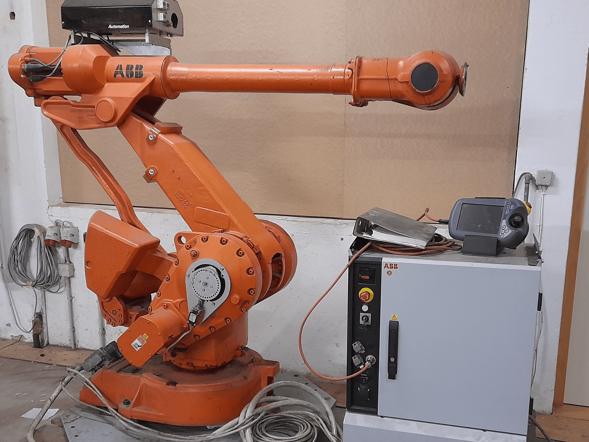 Oranžové robotické rameno ABB s ovládacím panelem, pohled zepředu, s kabely a automatizačním zařízením.