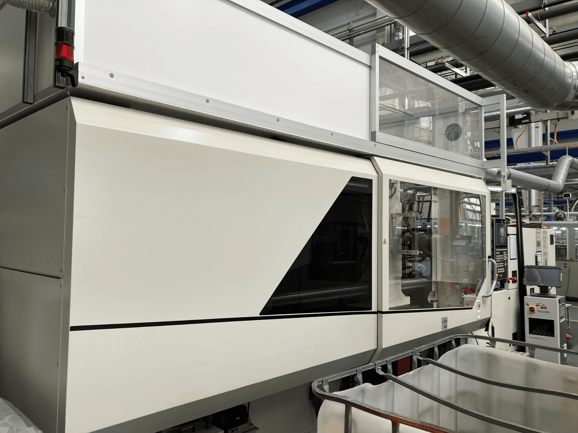 Průmyslový stroj s elegantním bílým designem, panelem displeje a skleněnou částí pro viditelnost součástí.