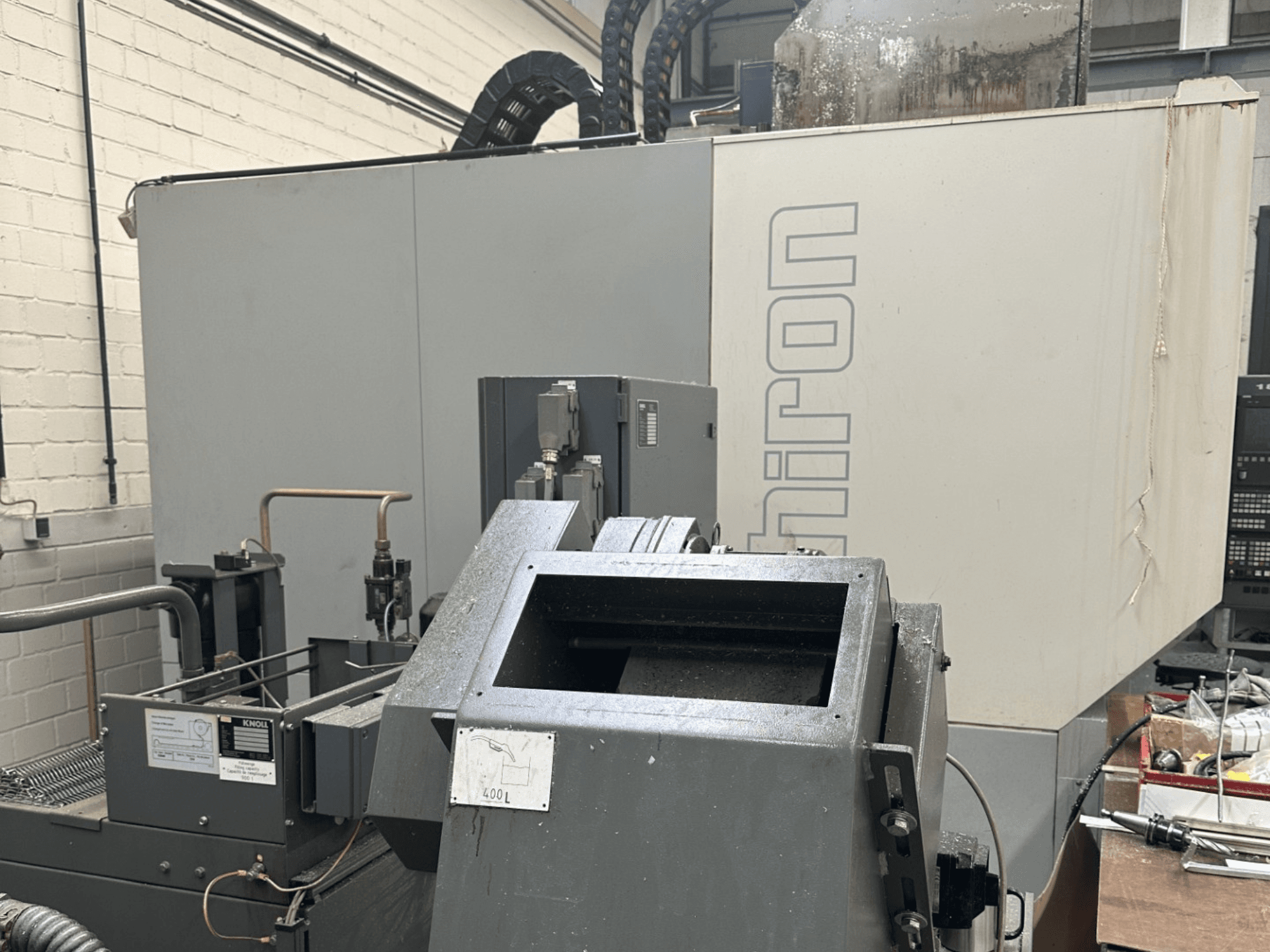 ZNAČKA: Chiron; Pohled zepředu na průmyslový CNC stroj s šedým exteriérem, viditelným ovládacím panelem a zaostřenými součástmi stroje.