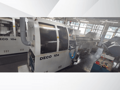 CNC stroj DECO 10a v dílně, pohled zepředu, ovládací panel a výfukový systém. Vyznačuje se robustní konstrukcí a přesnými nástroji.