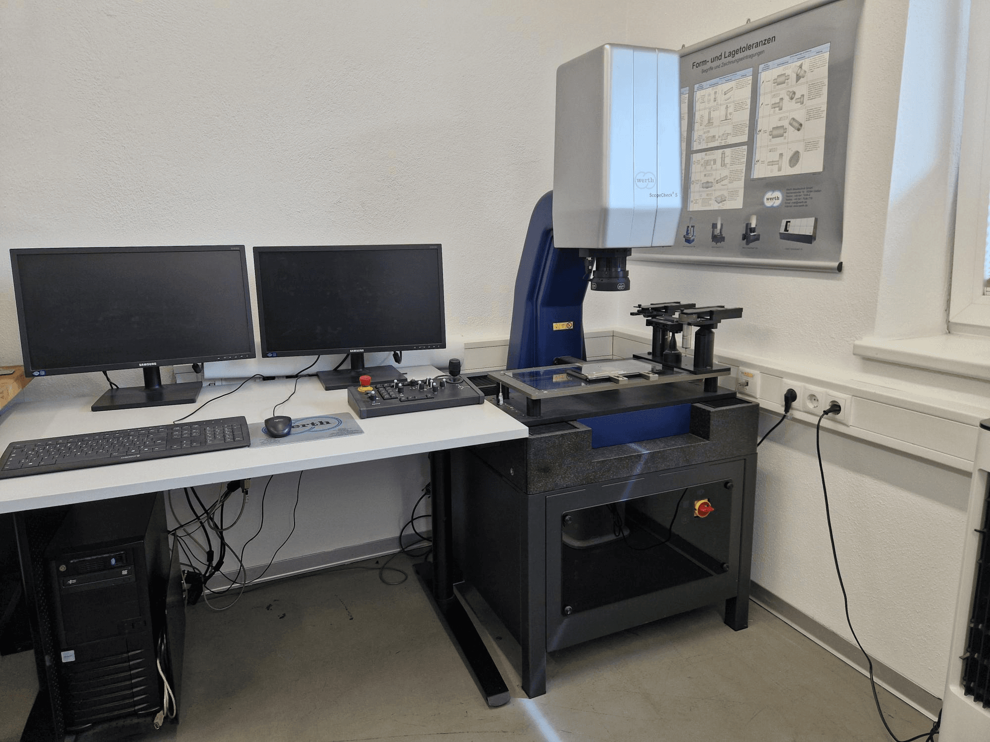 Souřadnicový měřicí stroj Werth Scopecheck 300S v laboratorním uspořádání; obsahuje měřicí stůl, dva monitory a ovládací panel.