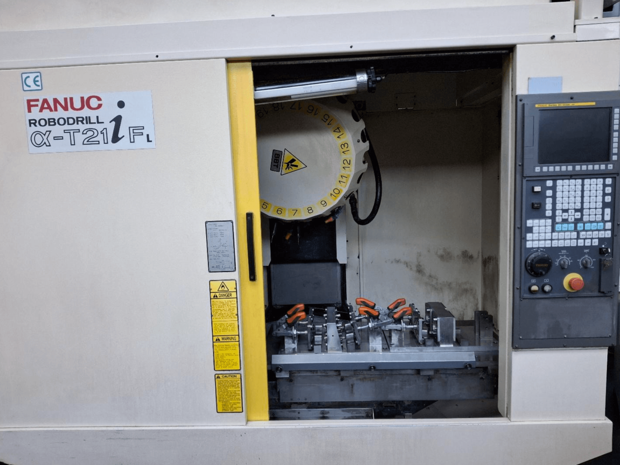 Vertikální obráběcí centrum FANUC ROBODRILL α-T21iFL z čelního pohledu, zobrazující nástroje a ovládací prvky uvnitř skříně stroje.