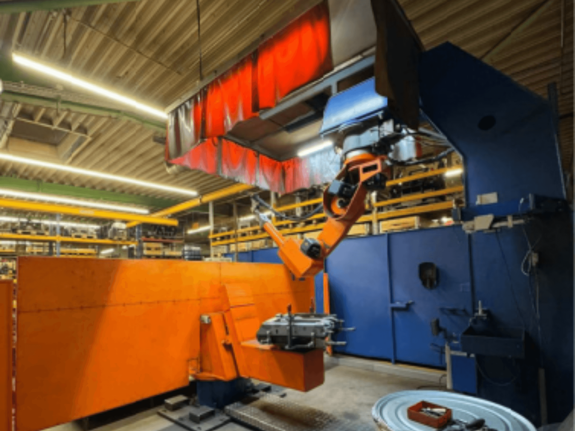 Svařovací robot CLOOS Romat 350 e v průmyslovém prostředí, pohled zepředu s oranžovým ramenem, držícím obrobek pod horní clonou.