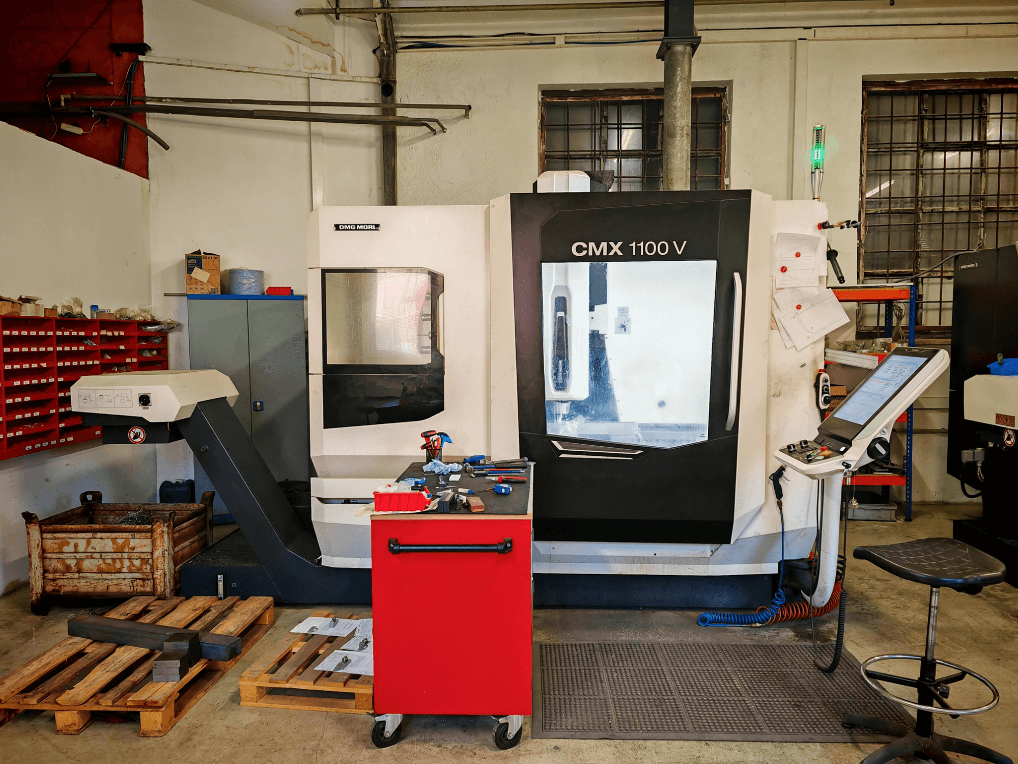 Vertikální obráběcí centrum DMG MORI CMX 1100 V v dílně, pohled zepředu, na kterém je vidět ovládací panel a okolní nástroje.