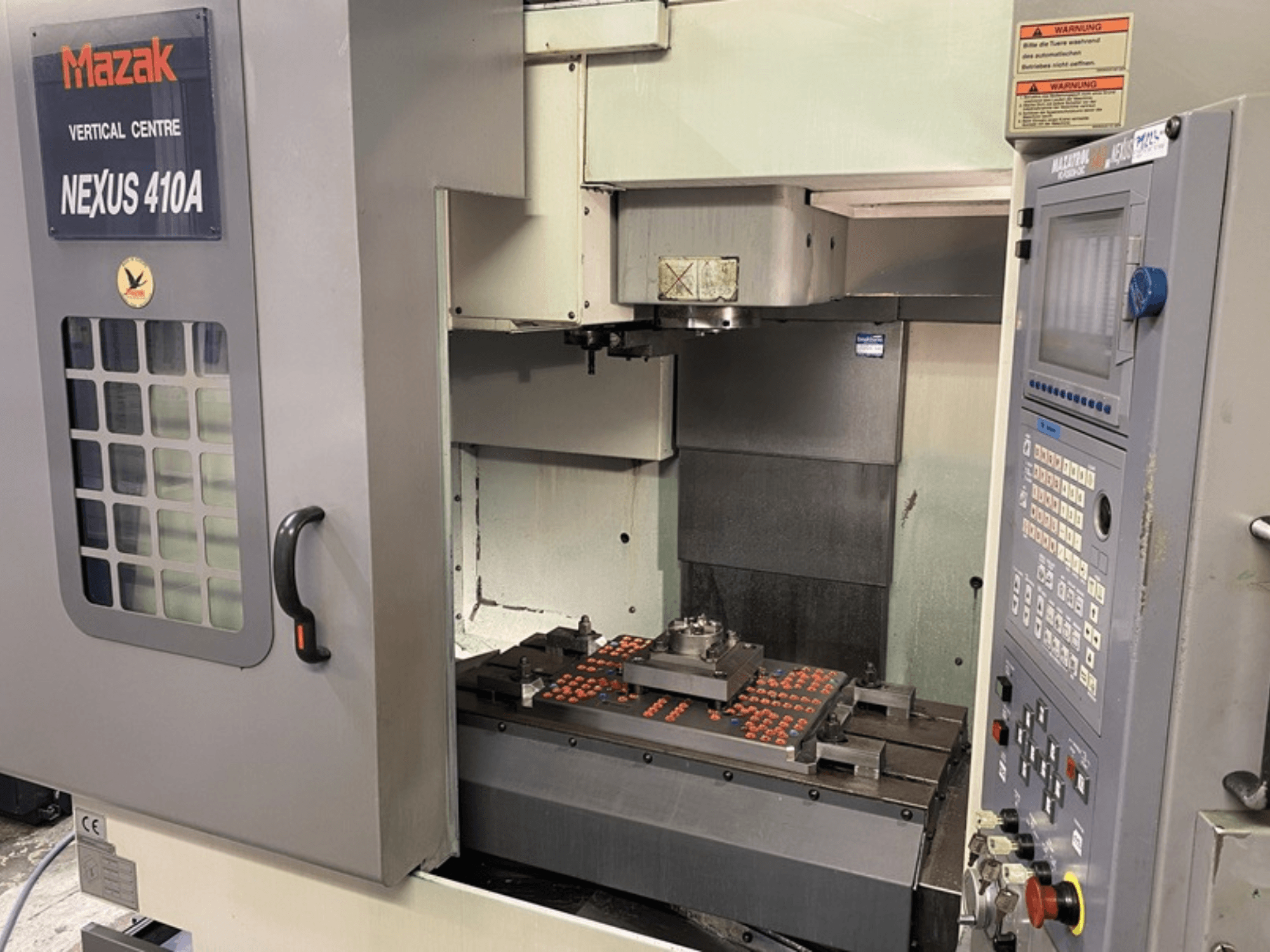 Vertikální obráběcí centrum Mazak VCN410, čelní pohled zobrazující ovládací panel a vnitřní prostor stroje s namontovaným obrobkem.