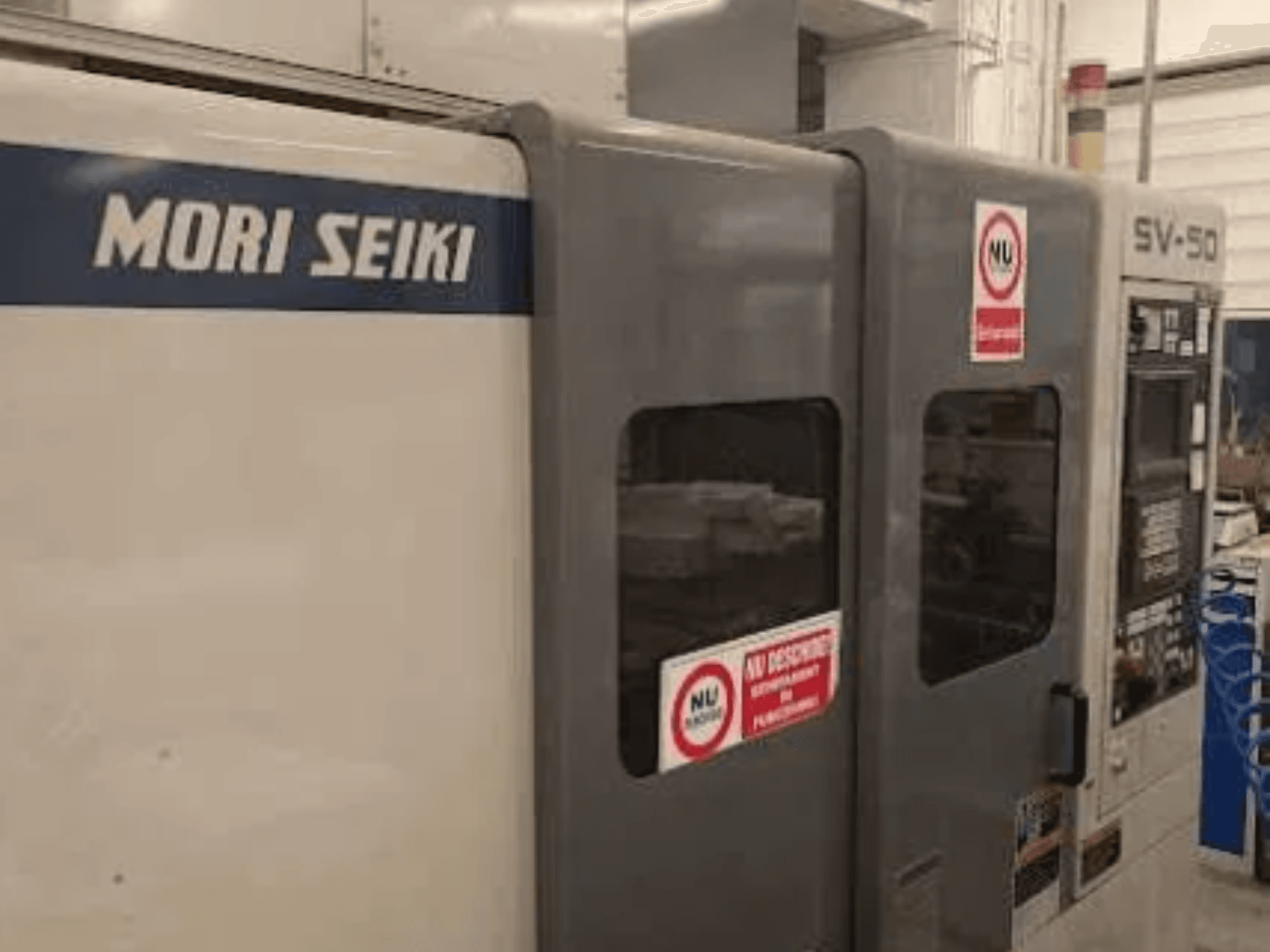 CNC stroj MORI SEIKI SV-50, pohled z boku; ovládací panel a bezpečnostní výstražné nálepky.