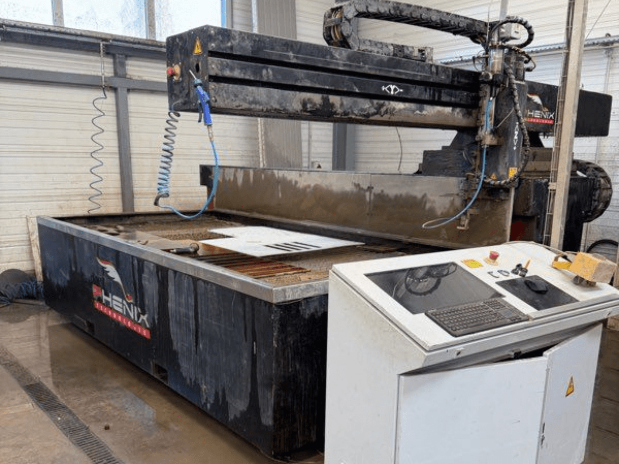 Řezací stroj PHENIX MD JET 1530 s vodním paprskem, pohled zepředu ukazuje ovládací panel a řezací prostor s viditelnou nádrží na vodu.