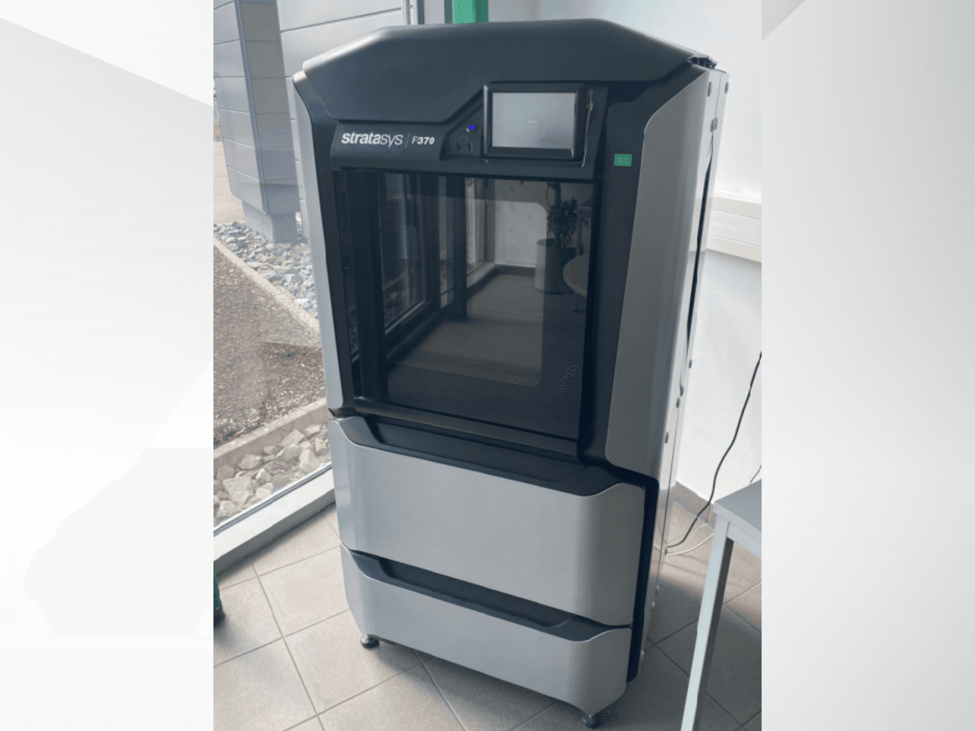 Plastová 3D tiskárna Stratasys F370, pohled zepředu, elegantní černošedý design s dotykovým displejem.