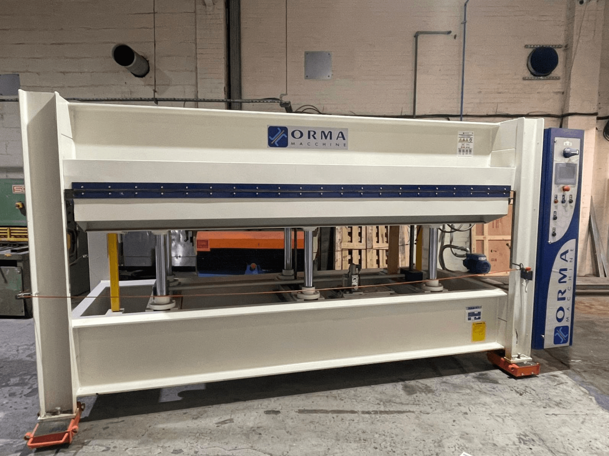 Hydraulický lis ORMA machinery, pohled zepředu, se stříbrným povrchem, ovládacím panelem vpravo a vzpřímenými písty pro lisování.