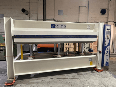 Hydraulický lis ORMA machinery, pohled zepředu, se stříbrným povrchem, ovládacím panelem vpravo a vzpřímenými písty pro lisování.