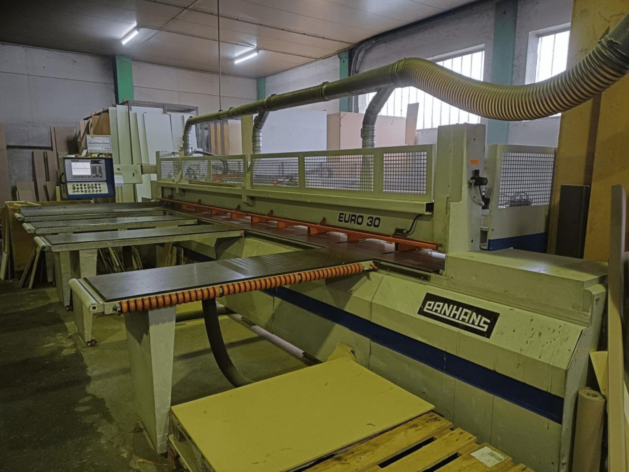 Pohled zepředu na panelovou pilu PANHANS EURO 30 s ovládacím panelem, řezacím stolem a hadicí pro odsávání prachu v dílně.