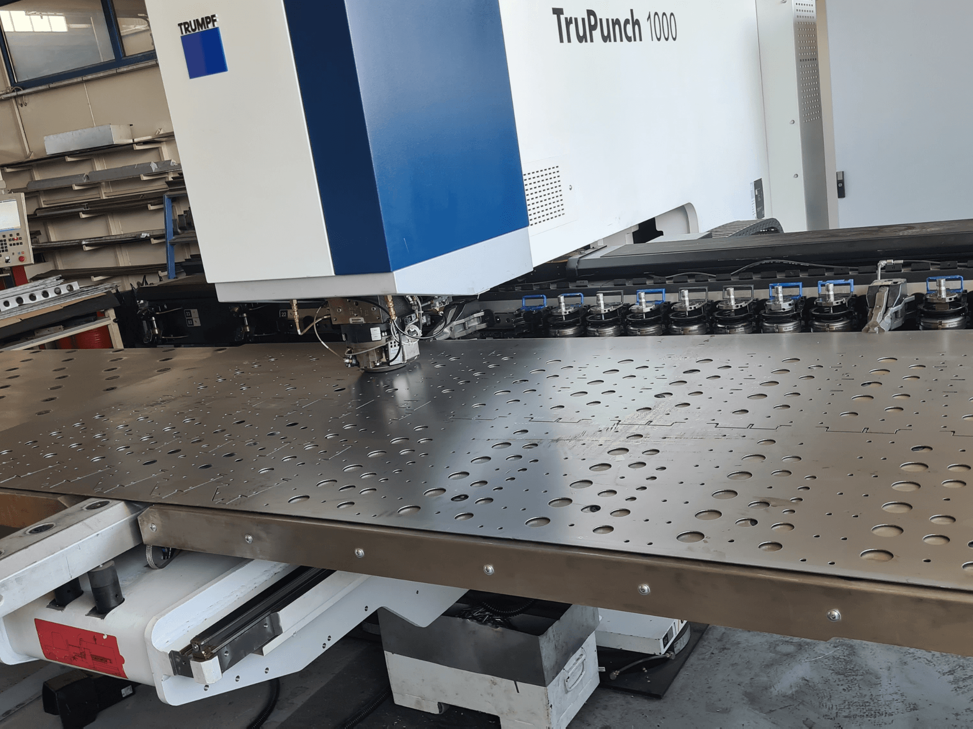 CNC děrovací stroj TRUMPF TruPunch 1000, pohled zepředu, s perforovaným plechem a nastaveným nástrojem.