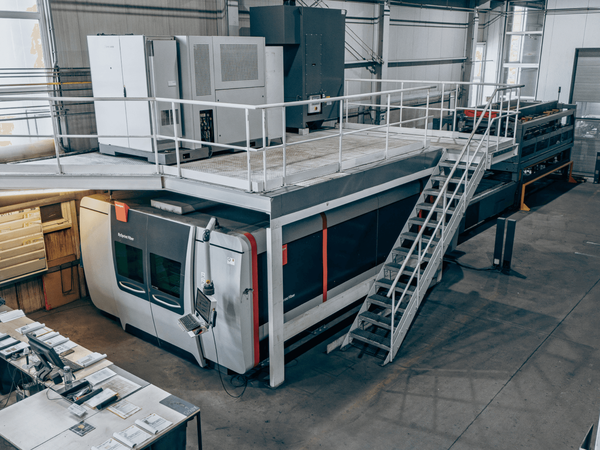 Vláknový laserový řezací stroj Bystronic BySprint Fiber 4020 s modulem ByTransExtended 4020, pohled shora, na kterém je vidět ovládací panel a schody.
