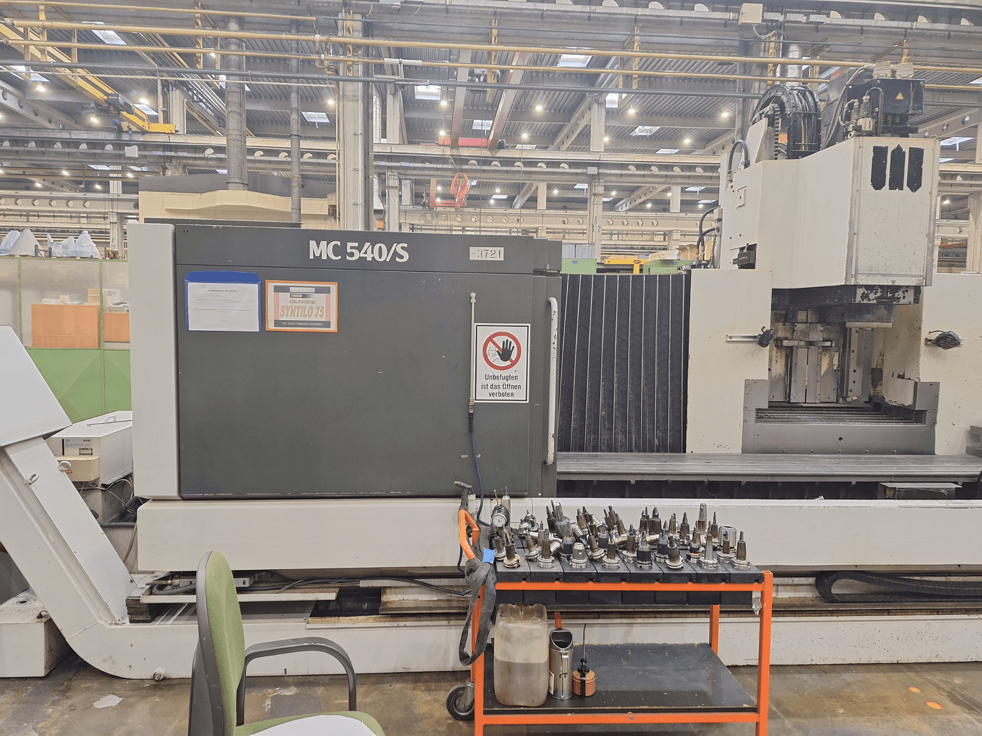 Vertikální obráběcí centrum STAMA MC 540S v dílně, boční pohled s držáky nástrojů na vozíku poblíž.