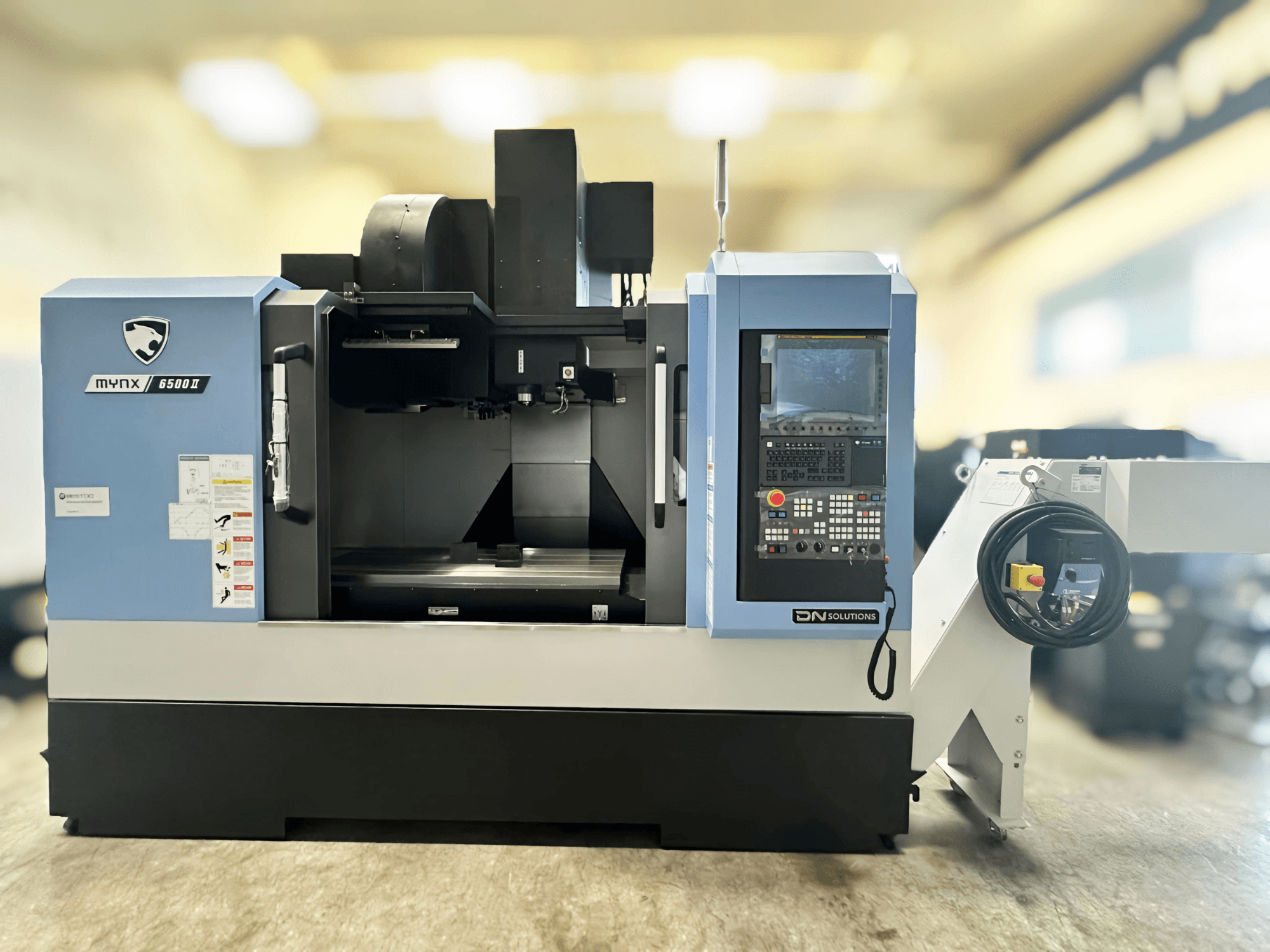 Vertikální obráběcí centrum DN SOLUTIONS MYNX 6500 II, pohled zepředu na ovládací panel a otevřený obráběcí prostor.