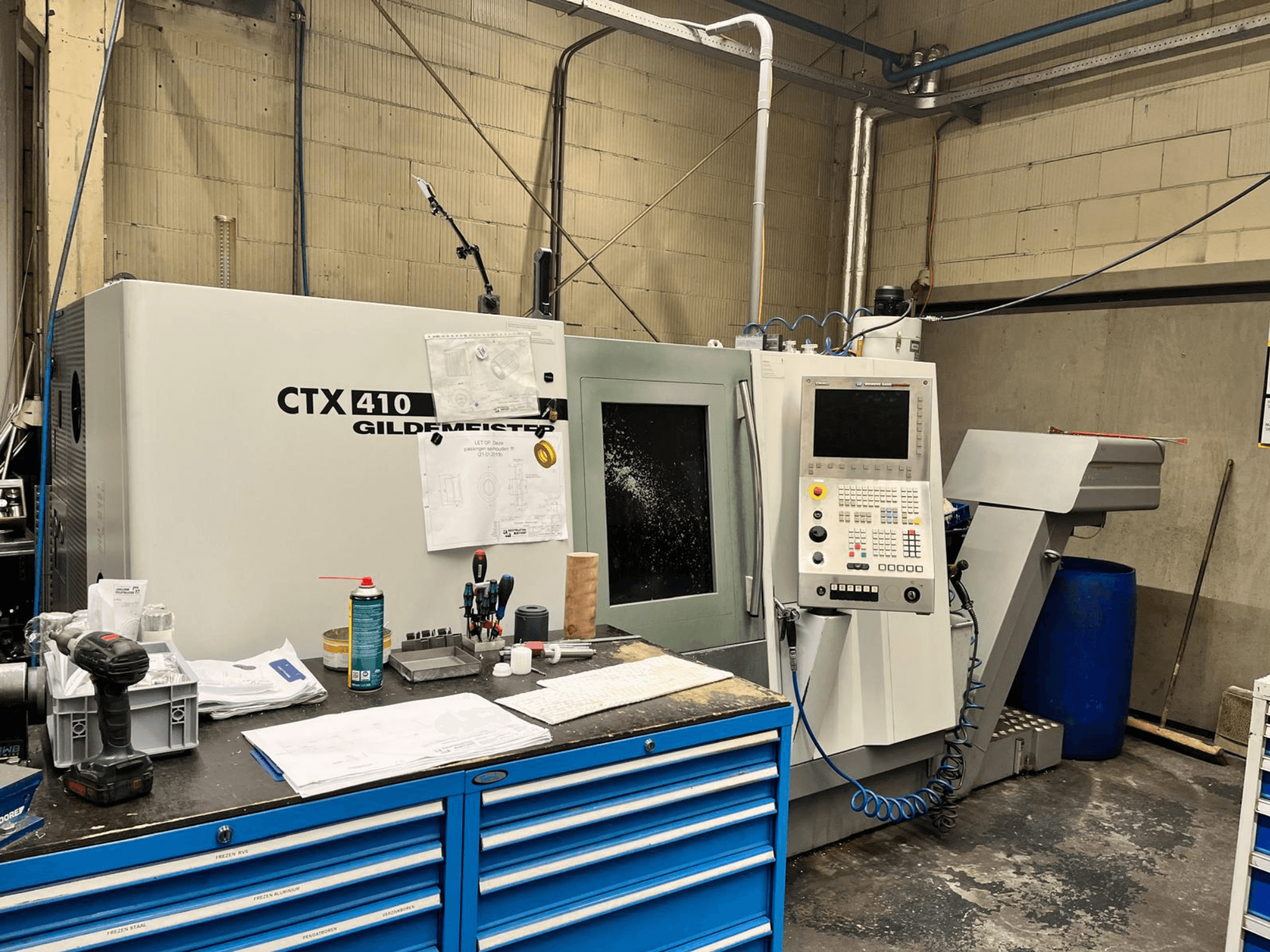 CNC stroj Gildemeister CTX 410 v dílně, pohled zepředu, s ovládacím panelem a různými nástroji na pracovním stole.
