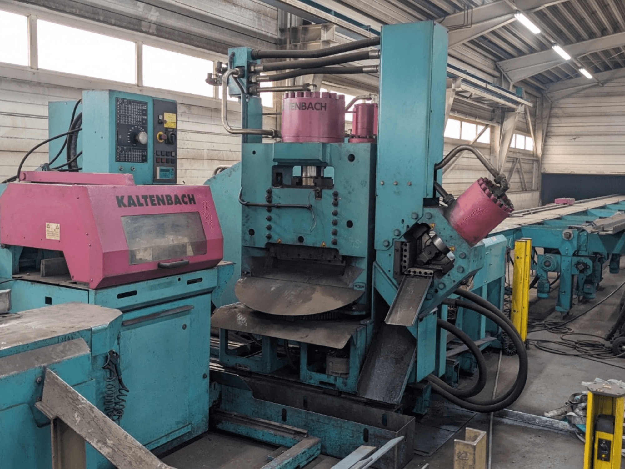 Průmyslový stroj KALTENBACH v tyalové a růžové barvě, pohled zepředu, ovládací panel a hydraulické komponenty.
