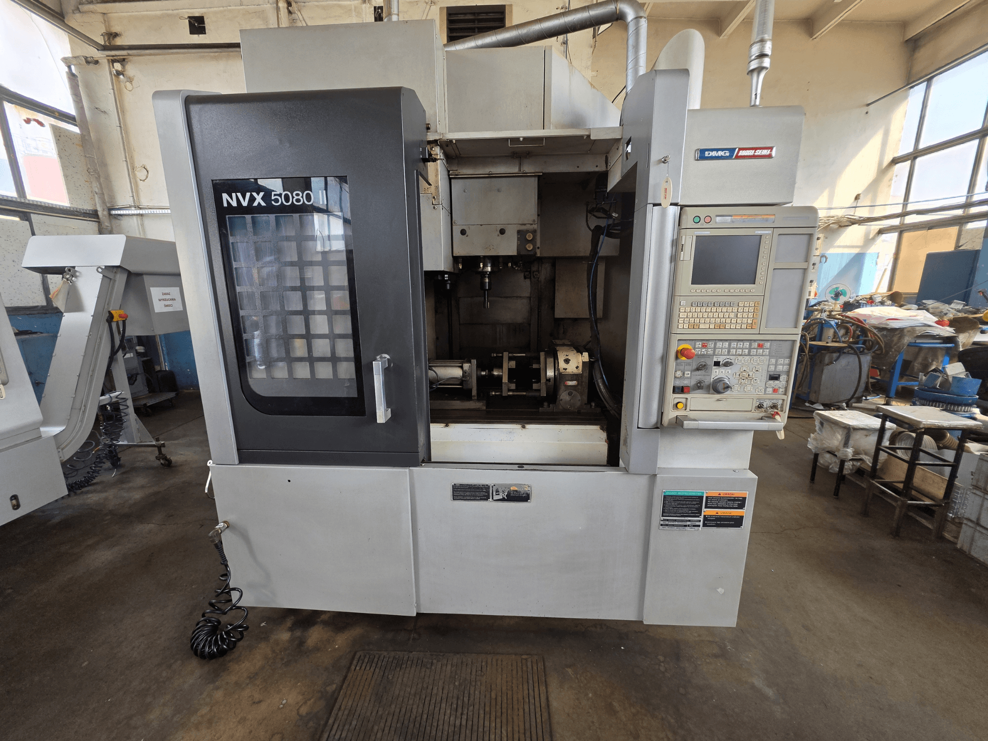 Pohled zepředu na vertikální obráběcí centrum DMG Mori Seiki NVX 5080 II/40 s ovládacím panelem a průhledným okénkem, které umožňuje nahlédnout do obráběcího prostoru.