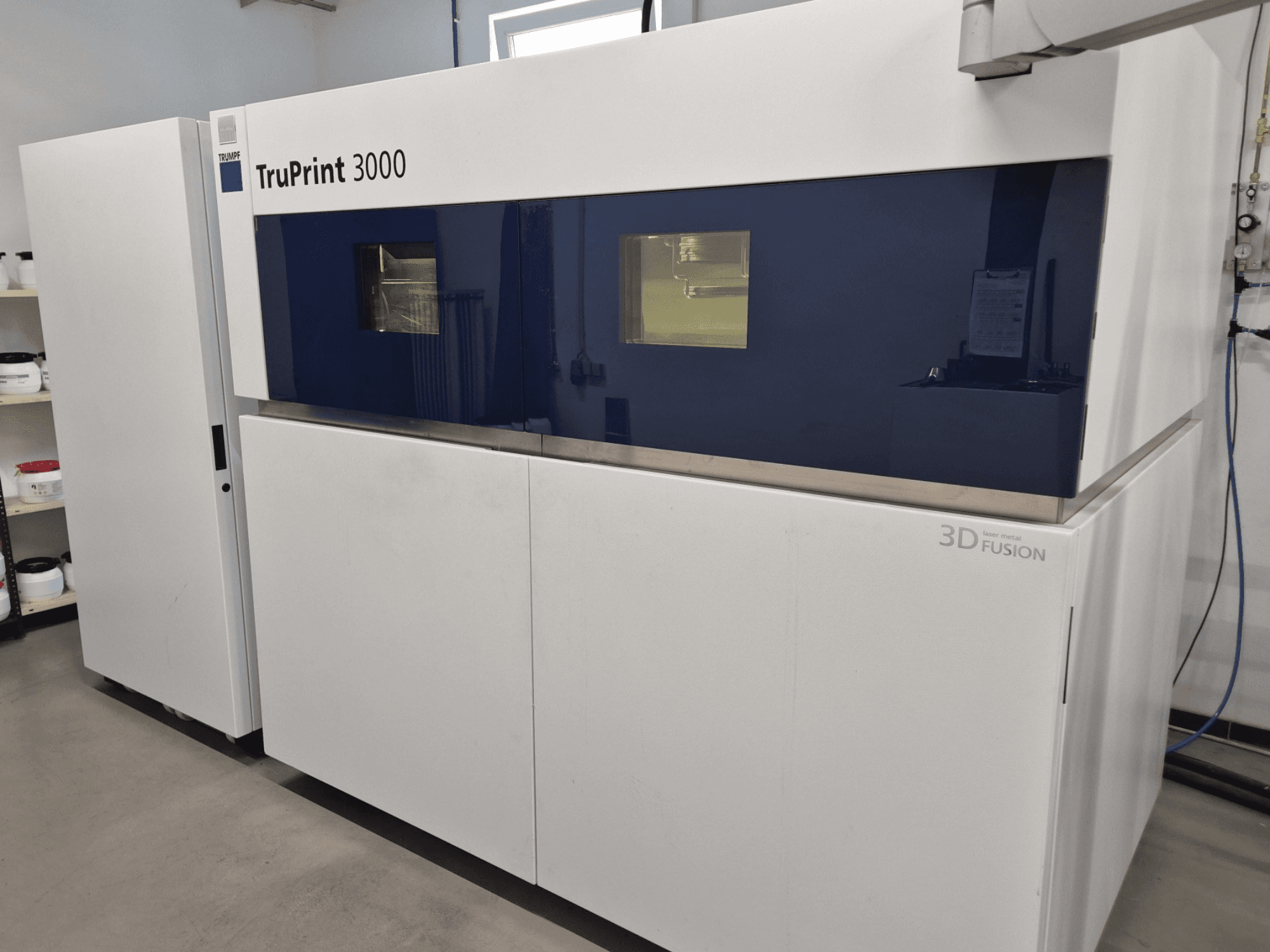 Kovová 3D tiskárna TruPrint 3000 v čelním pohledu, s modrým designem a technologií laserové fúze.