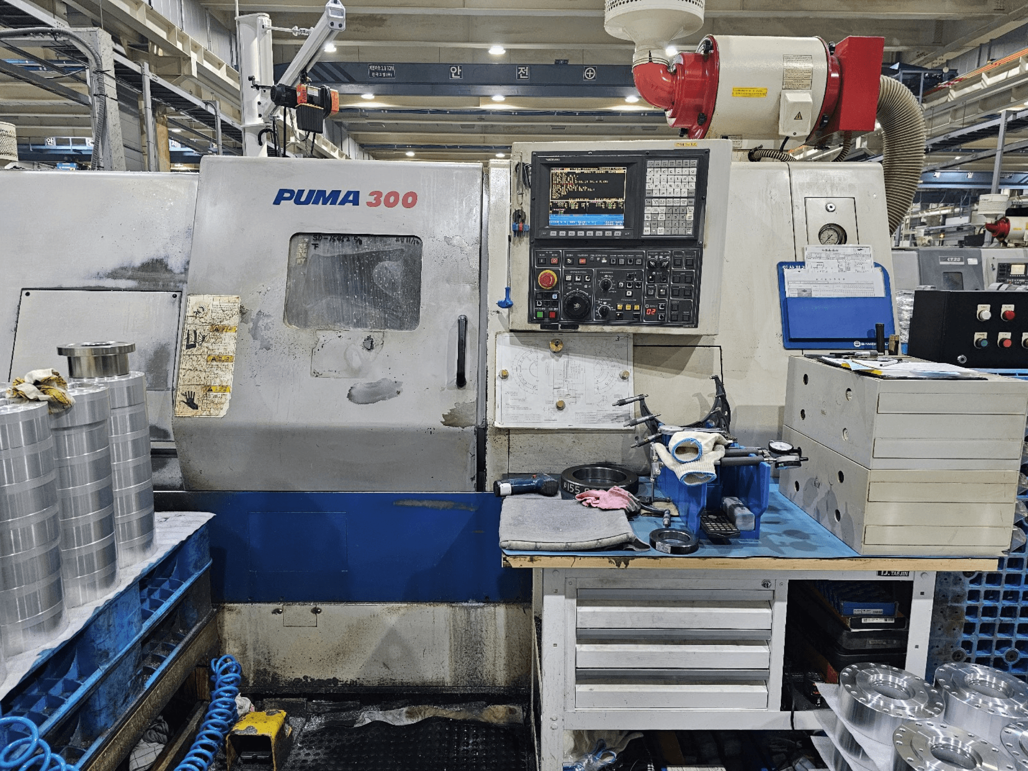 CNC stroj PUMA 300 v dílně; pohled zepředu ukazuje ovládací panel, nástroje a kovové díly na pracovním stole.