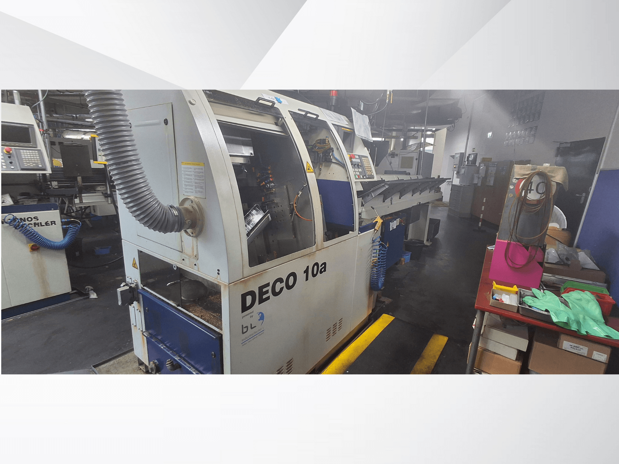 CNC stroj DECO 10a v dílně, pohled zepředu; s ovládacím panelem a systémem odsávání prachu, s pracovním stolem v blízkosti.