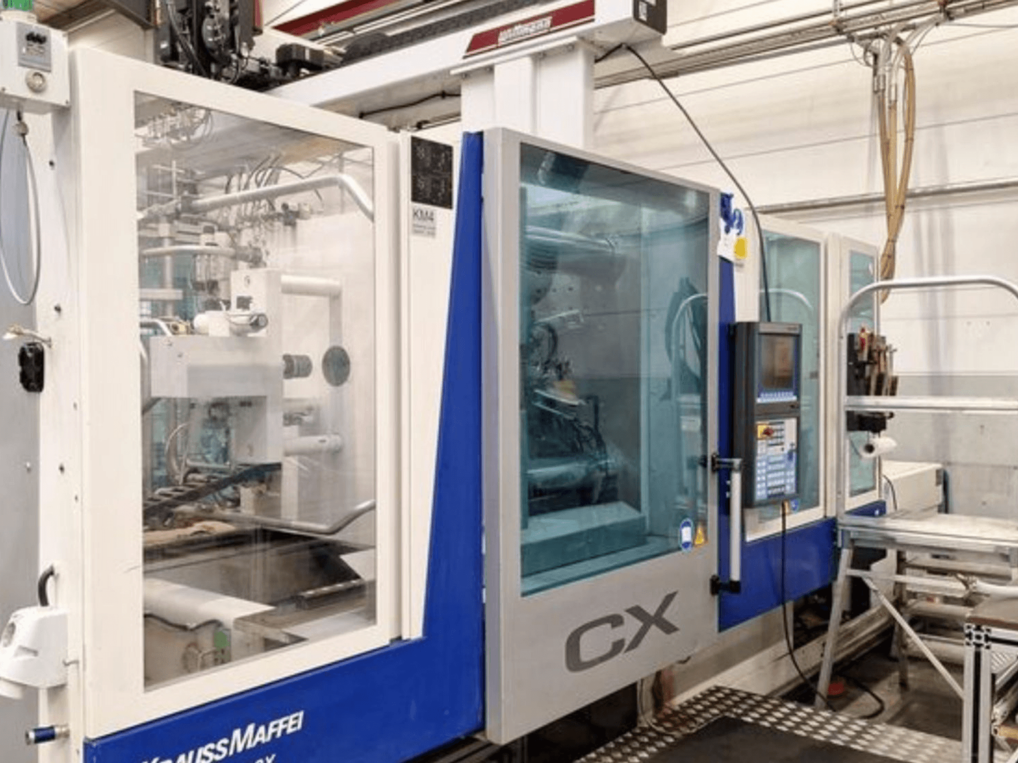Hydraulický vstřikovací lis Krauss Maffei 300-1400 CX, boční pohled, na kterém je vidět ovládací panel a průhledný kryt.