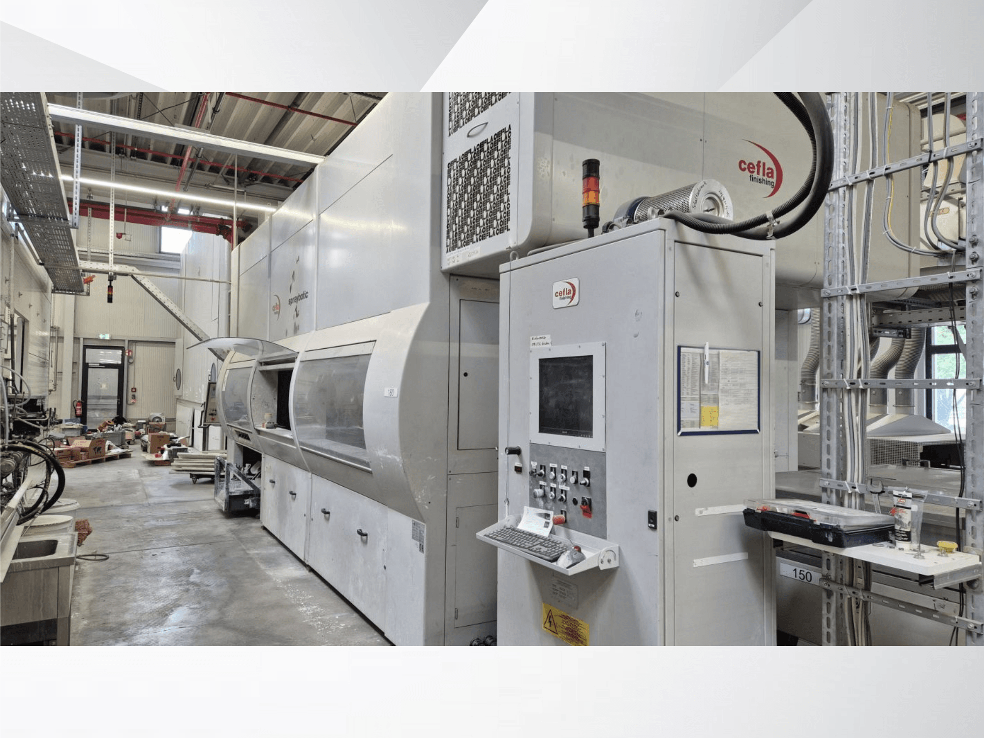 Výrobní linka Cefla Spraybotic MD v dílně, pohled zepředu znázorňující ovládací panel a stříkací komoru s průhledným krytem.