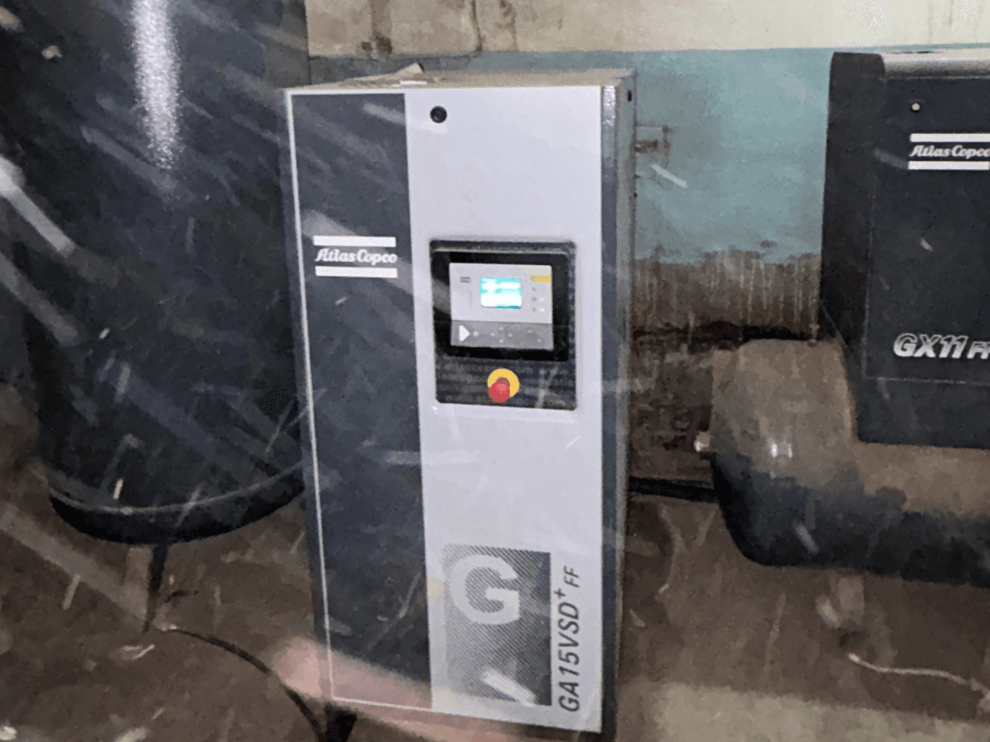Vzduchový kompresor Atlas Copco GA15VSD+FF, pohled zepředu, včetně ovládacího panelu s displejem a červeným tlačítkem nouzového zastavení.