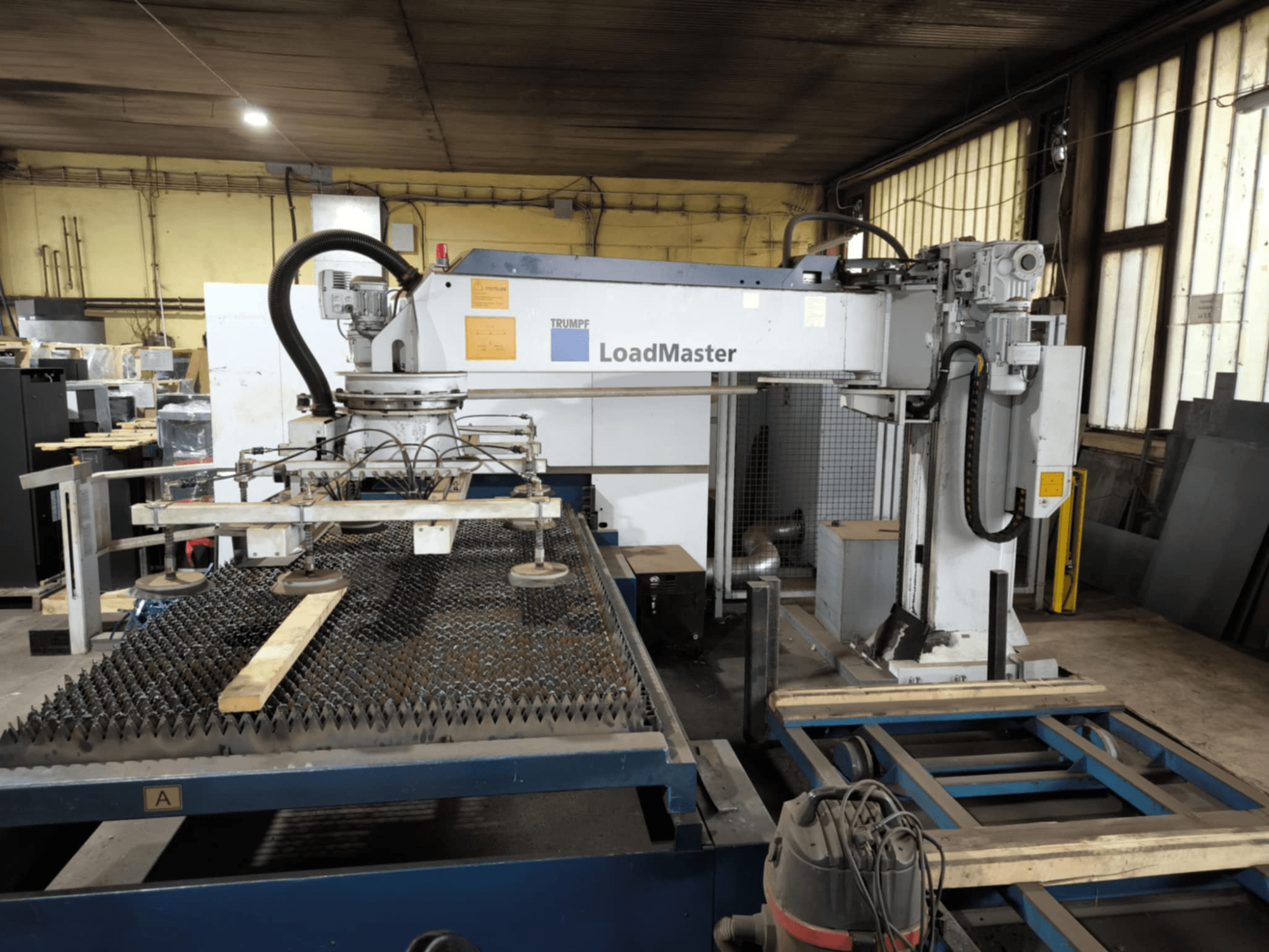 Řezací stroj TRUMPF TRULASER 3030 FIBER, pohled zepředu, se systémem LoadMaster a umístěný na roštovém pracovním stole.