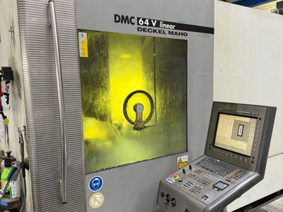 DMC 64 V lineární od Deckel Maho, čelní pohled na stroj s ovládacím panelem a žlutě tónovaným okénkem ukazujícím vnitřní mechanismy.