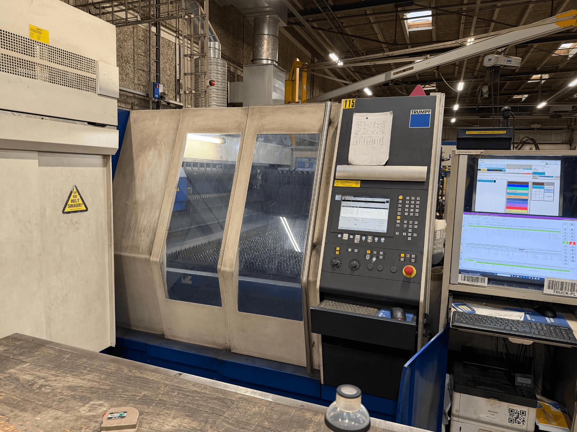 Pohled zepředu na průmyslový laserový stroj Trumpf s ovládacím panelem a digitálními displeji v továrním prostředí.