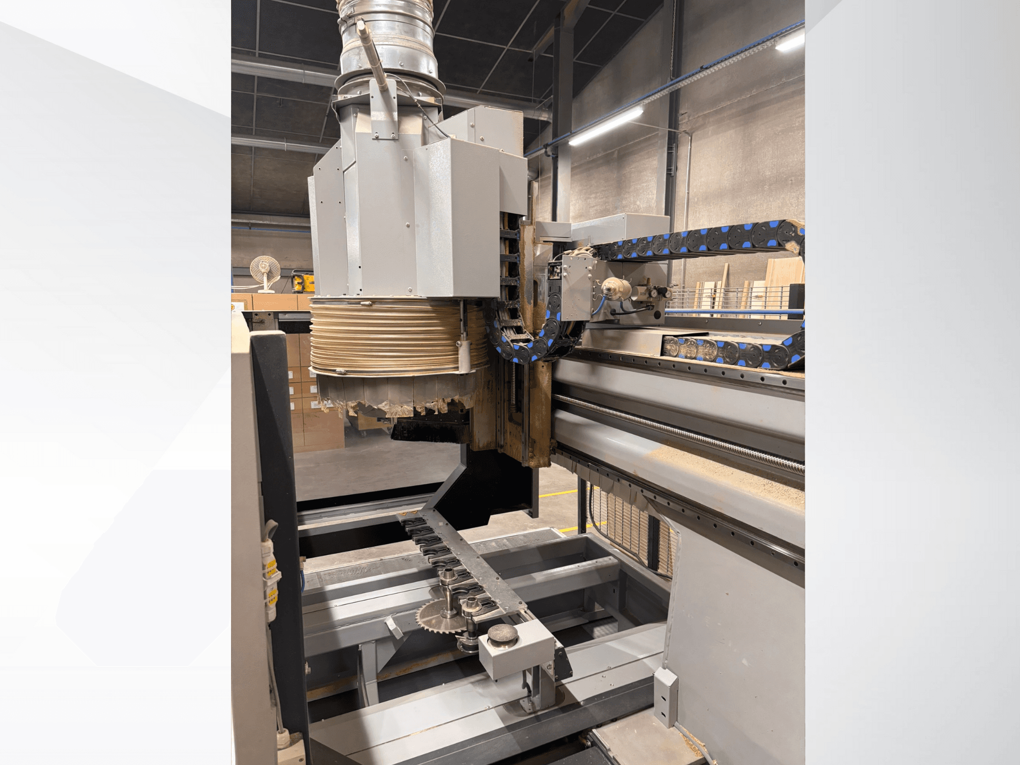 CNC frézka s velkým vřetenem a dopravníkem, boční pohled, zobrazení nástrojů na řezání dřeva a strojních součástí.