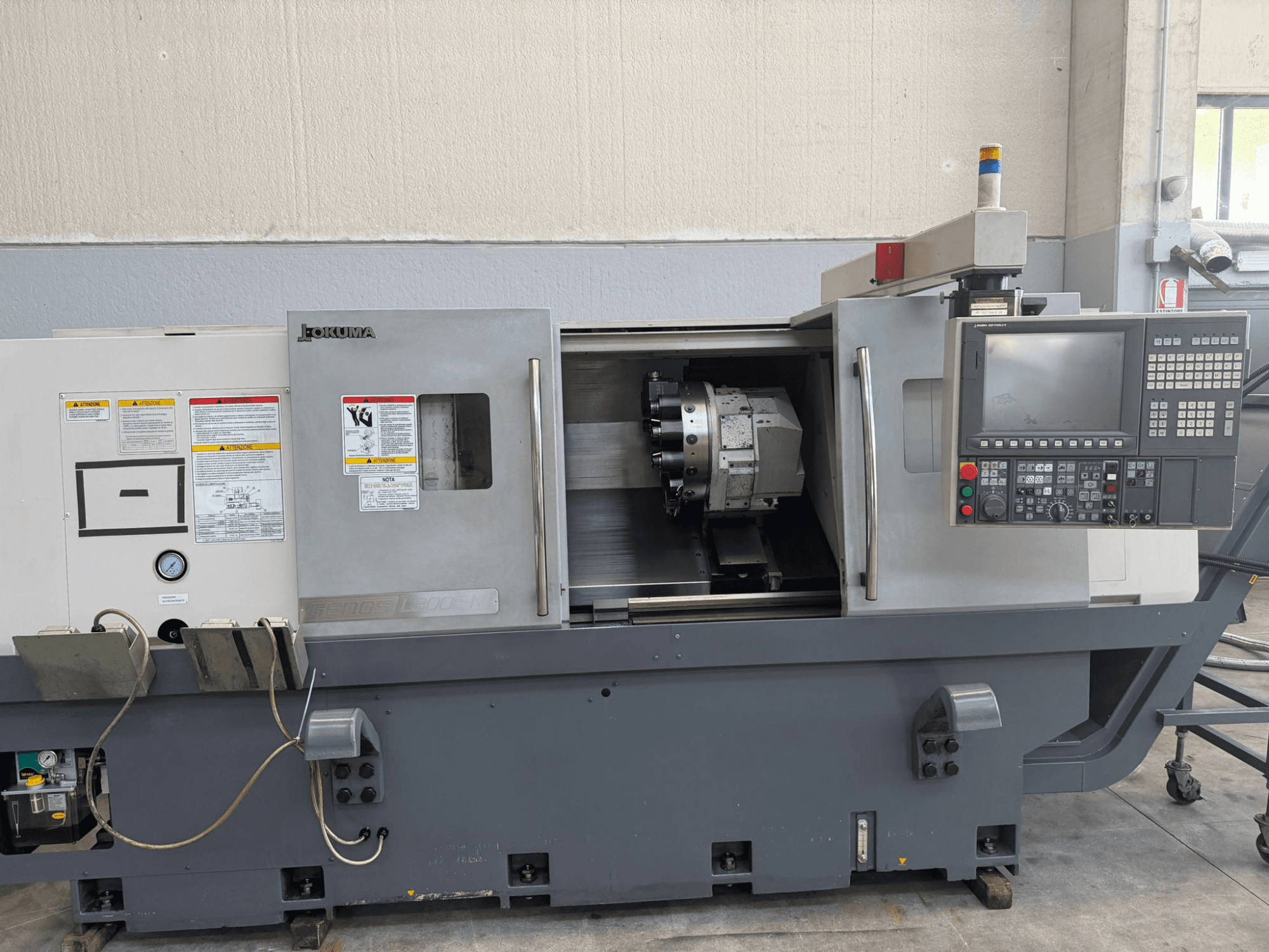 CNC soustruh Okuma, pohled zepředu, zobrazující ovládací panel, držák řezných nástrojů a bezpečnostní upozornění na boku.