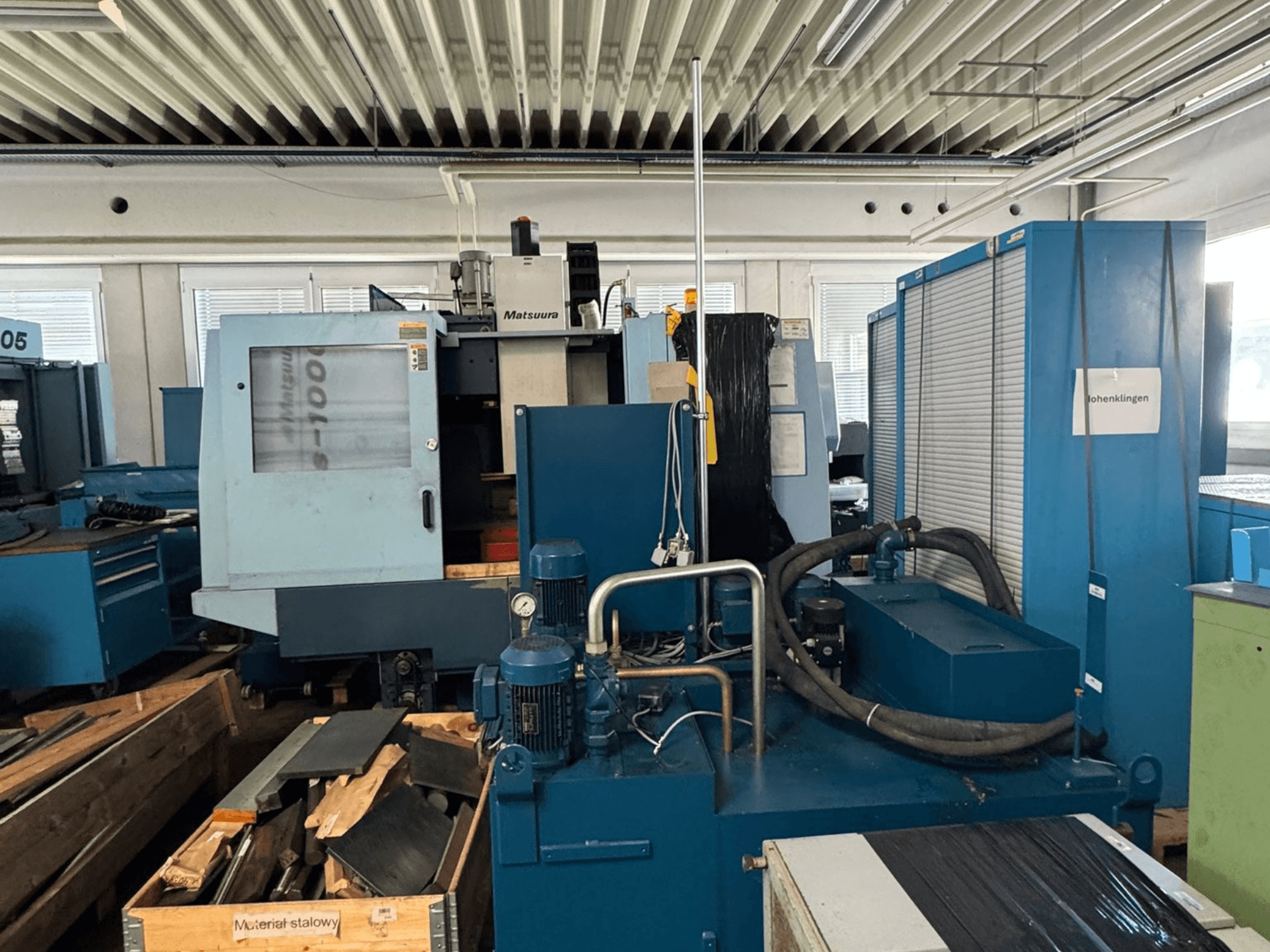 Pohled zepředu na vertikální obráběcí centrum Matsuura Vplus 1000/40, na kterém jsou vidět ovládací prvky, motory a okolní prostředí dílny.