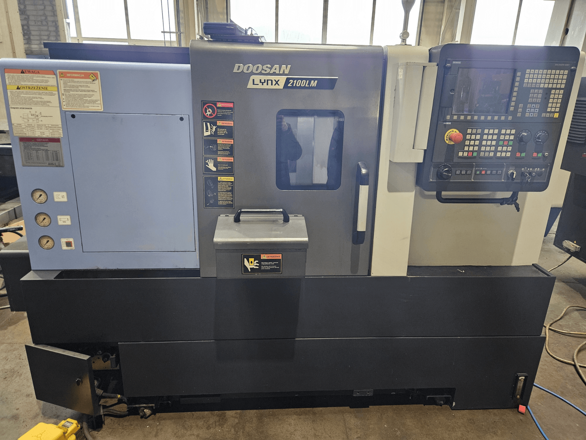CNC soustruh Doosan Lynx 2100LM, pohled zepředu, s viditelným ovládacím panelem, manometry tlaku vzduchu a bezpečnostními štítky.