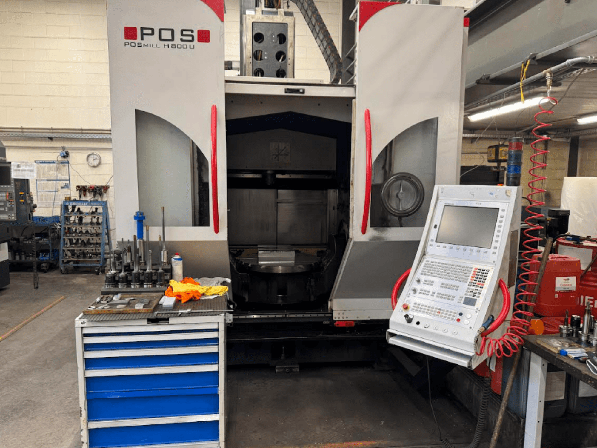 CNC stroj POSMILL H800 U při pohledu zepředu, kde je vidět ovládací panel a pracovní plocha s nástroji a zařízením v blízkosti.