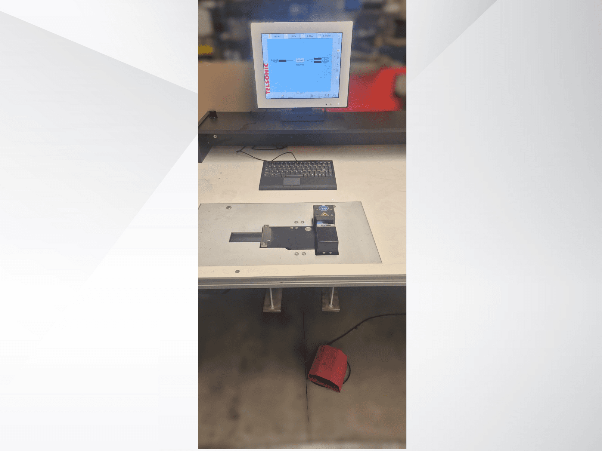 Pohled shora dolů na testovací stanici s počítačovým monitorem, klávesnicí a ovládacím panelem s tlačítkem a zeleným světlem.