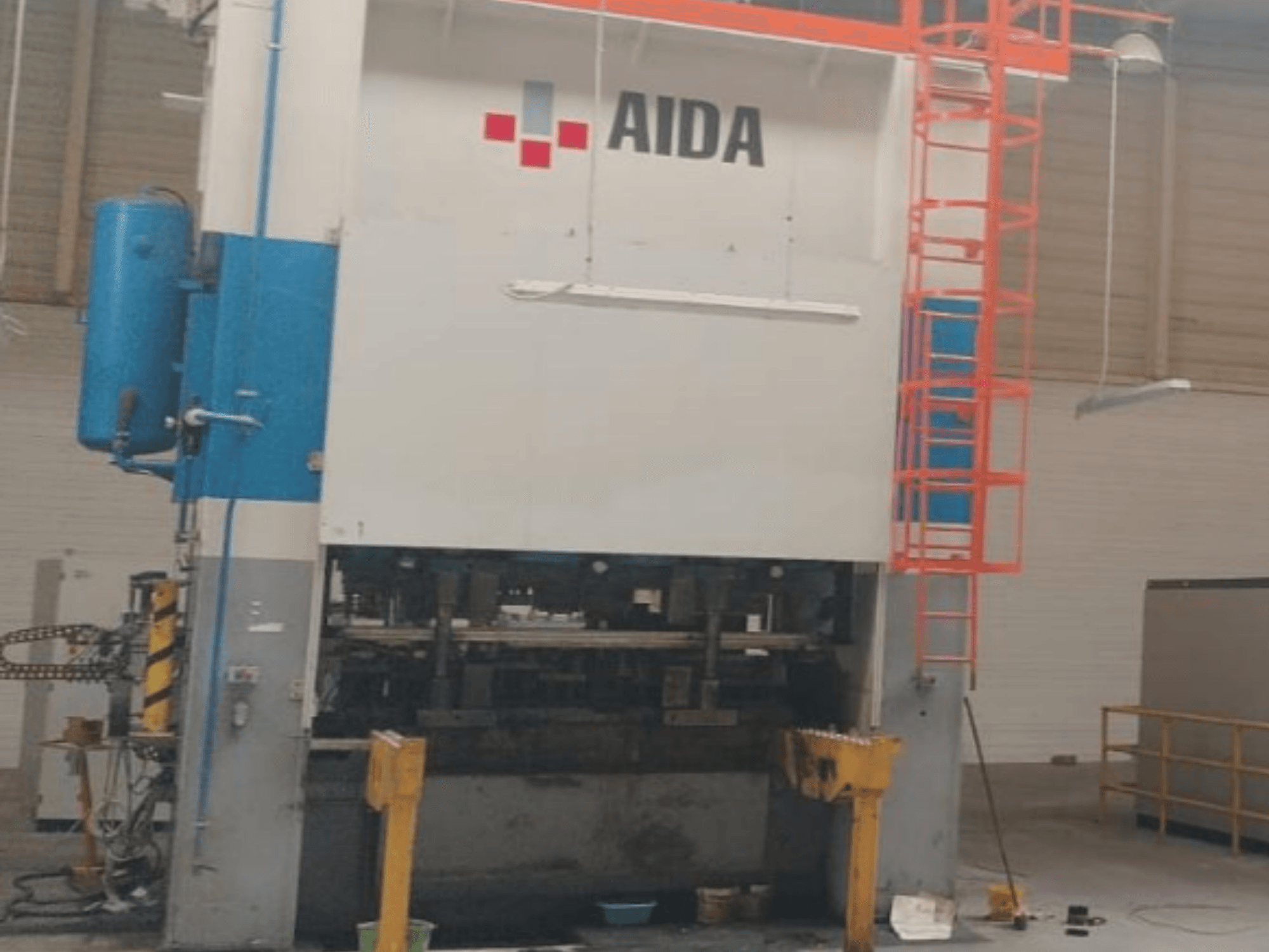 Mechanický lis AIDA 315/2MR/LD/TE3, pohled zepředu, hydraulické komponenty a bezpečnostní žebřík.