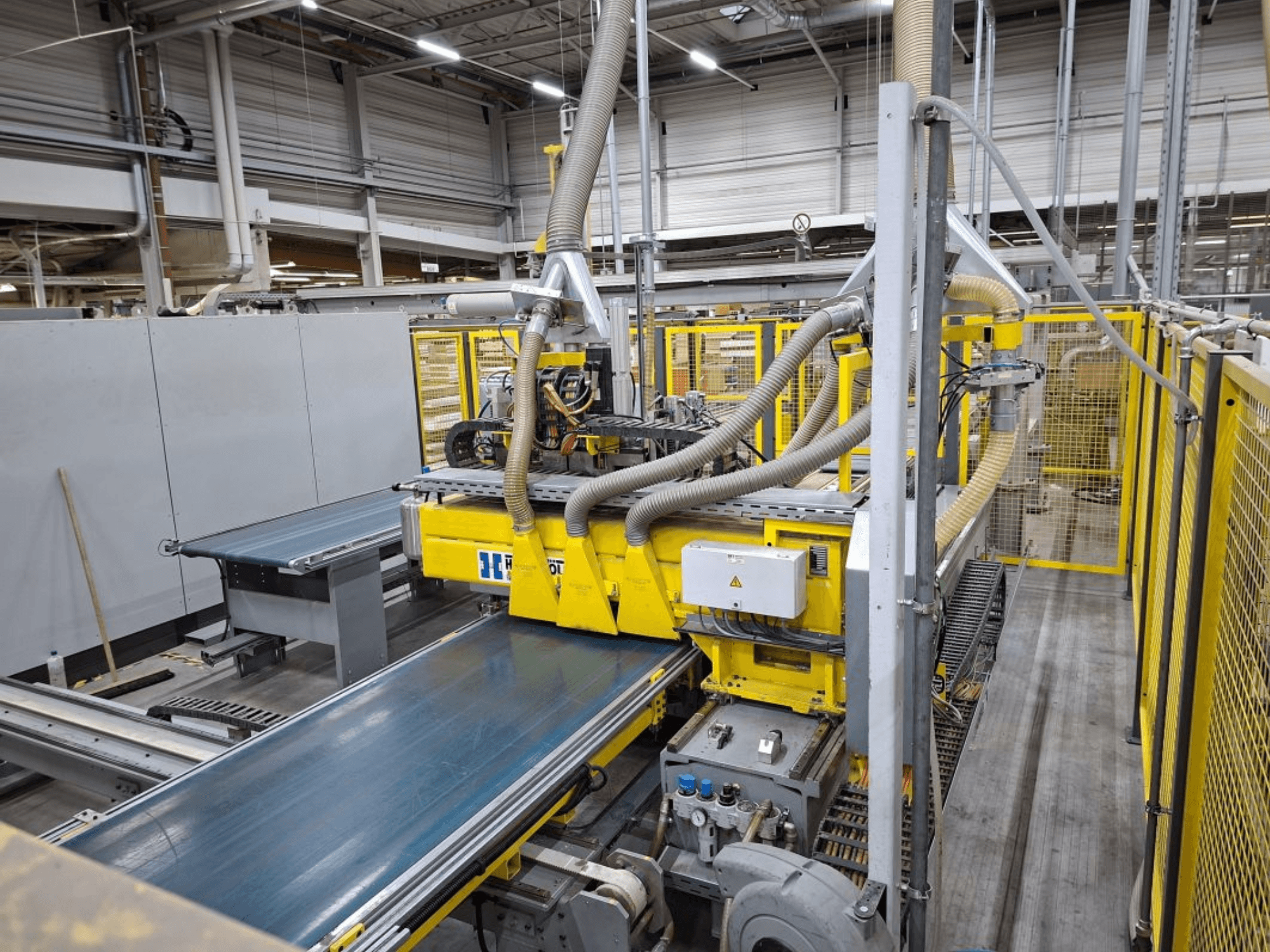 Průmyslový dopravní systém z bočního pohledu se žlutým strojním zařízením, ovládacím panelem a přípojkami pro výrobní hadice.