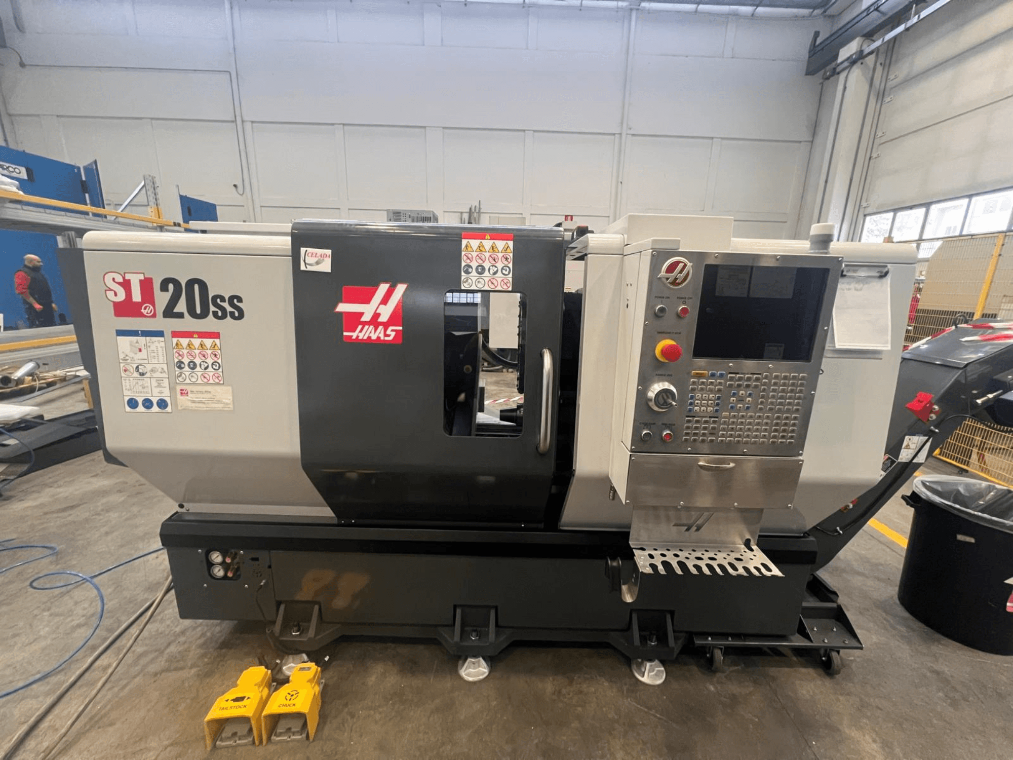 CNC soustruh Haas ST 20SS v bočním pohledu, s ovládacím panelem, bezpečnostními štítky a pedály na podlaze.