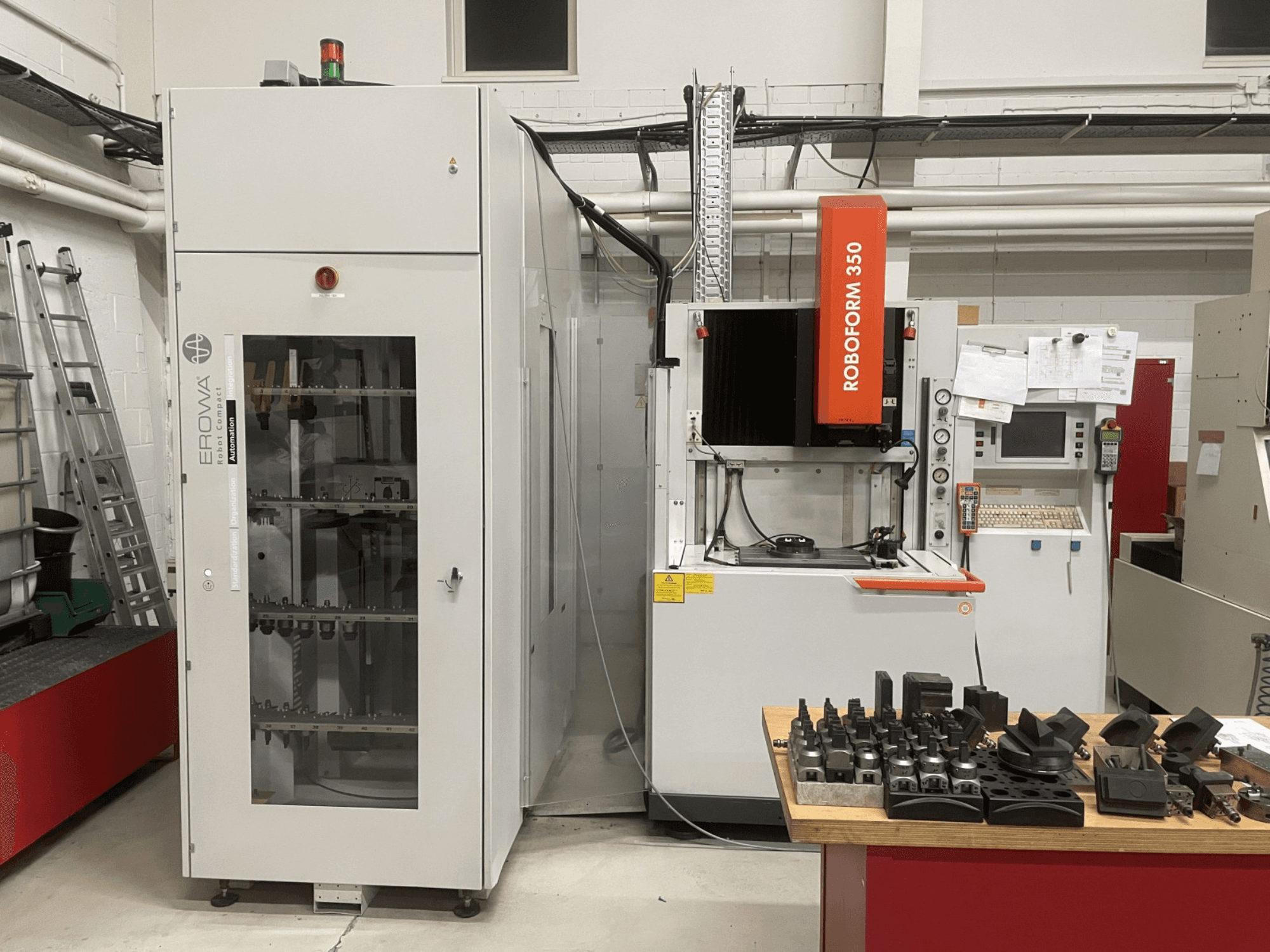 Hloubicí elektroerozivní stroj CHARMILLES Roboform 350, pohled zepředu, s nástroji zobrazenými na stole a přilehlým zařízením.