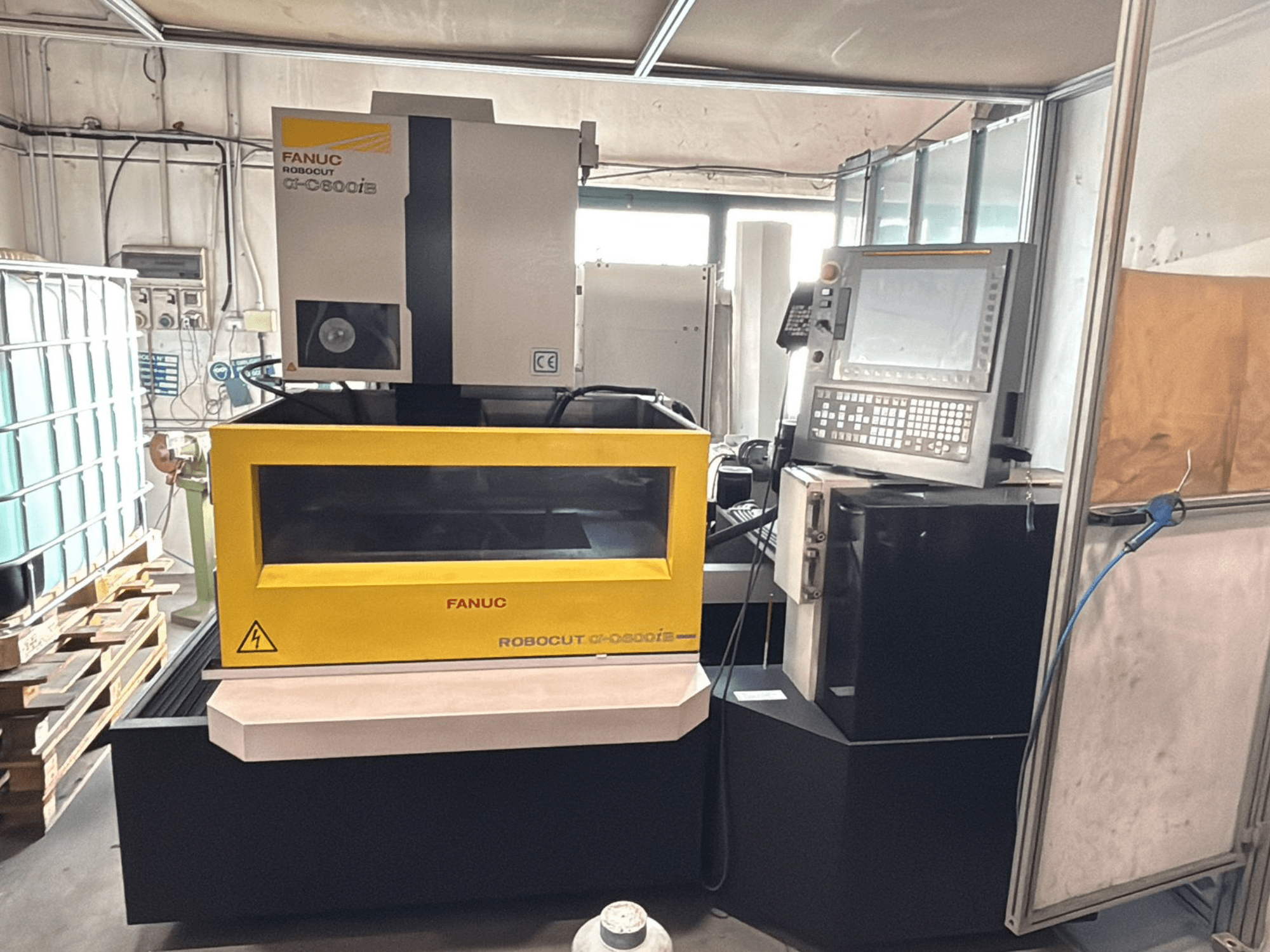 Pohled zepředu na CNC stroj FANUC Robocut α-0iE se žlutým krytem, na kterém je vidět ovládací panel a displej.