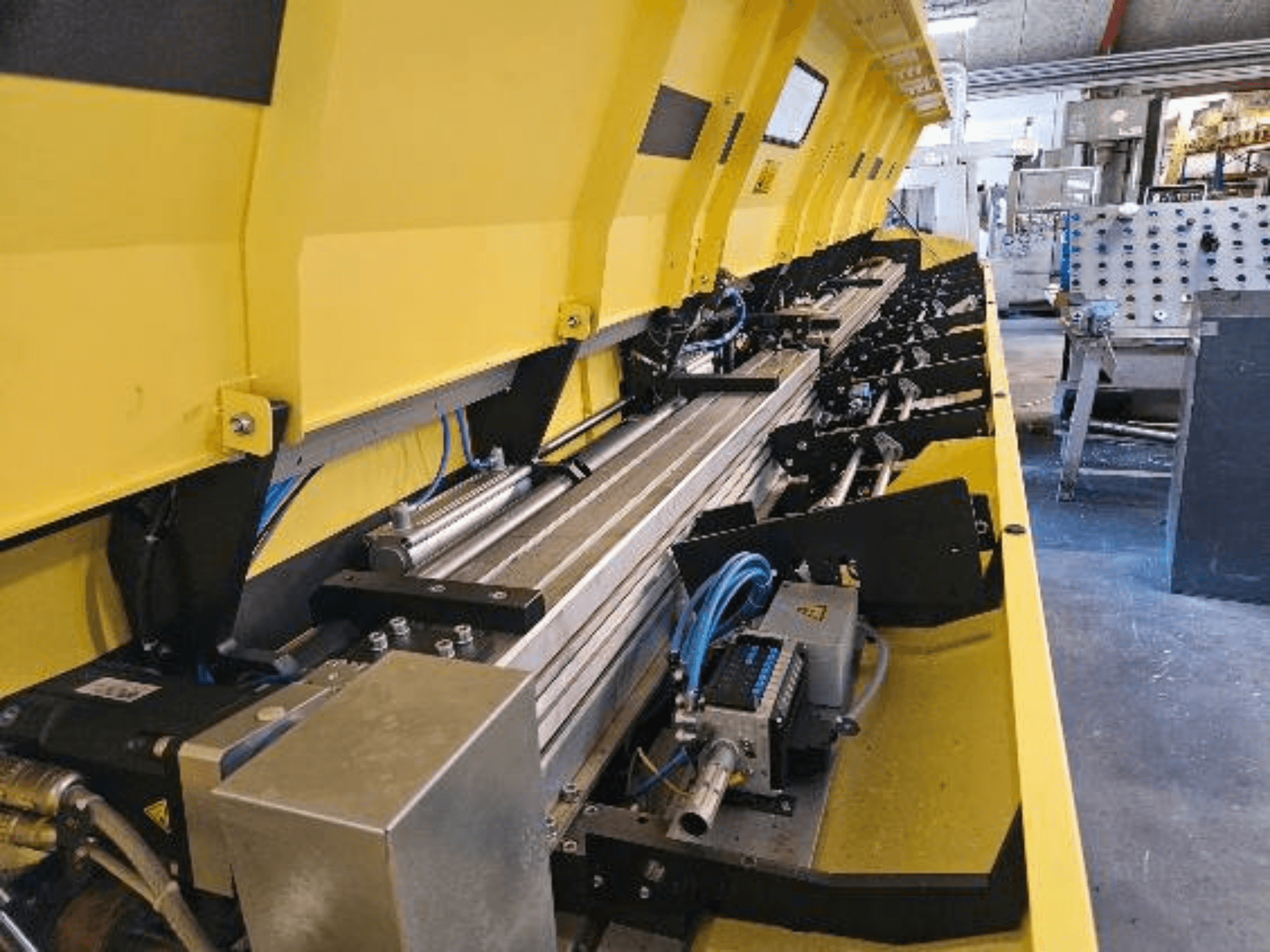 Pohled zblízka na žlutý hydraulický stroj s kovovými součástmi a dopravními pásy, s hadicemi a elektronickými součástmi.