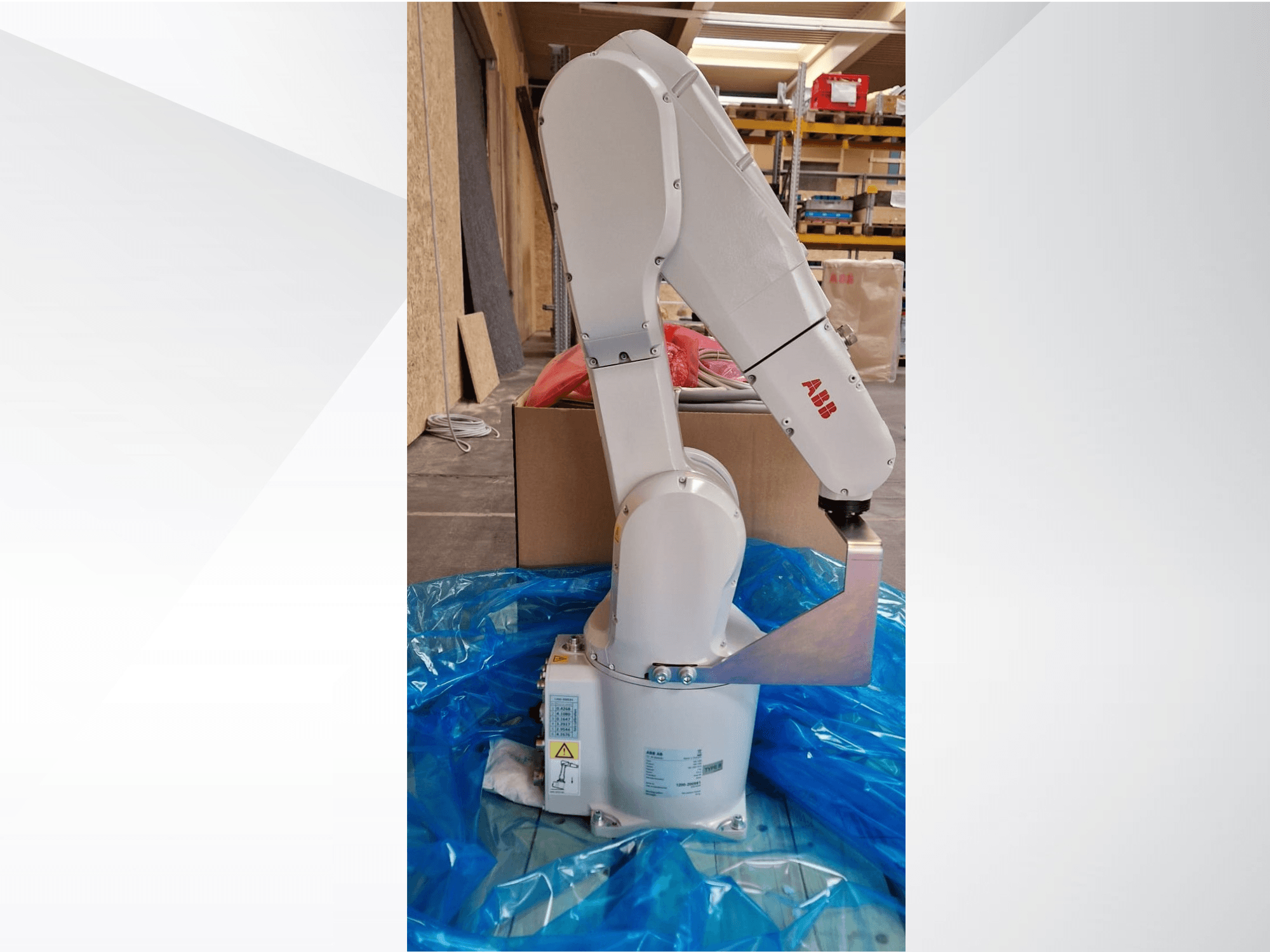 Model robotického ramene ABB, boční pohled na modrou plachtu, kloubové spojení a kovový koncový efektor, s viditelnými technickými štítky.
