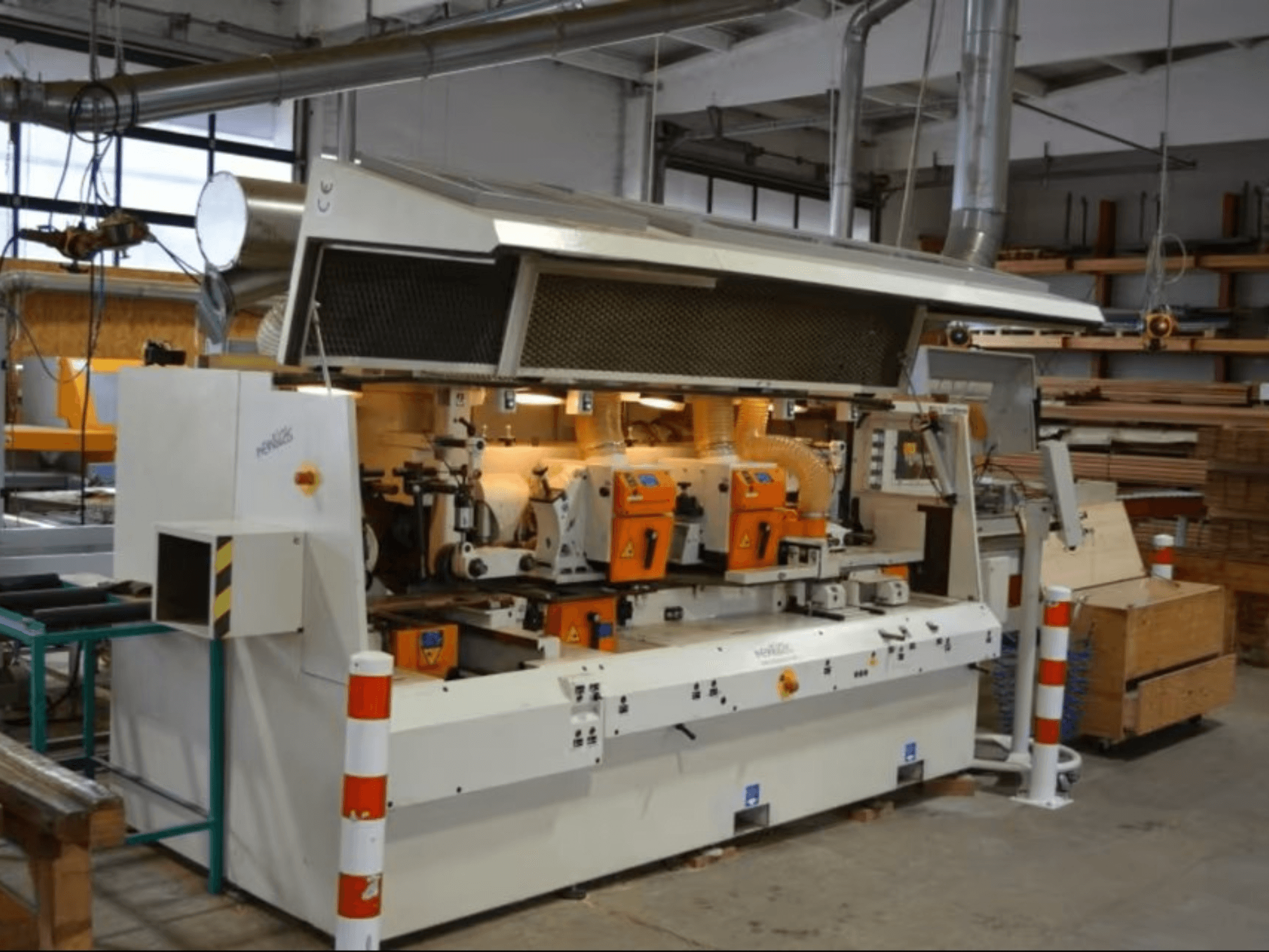 Stroj na zpracování dřeva PENIGAS, pohled zepředu, se dvěma oranžovými řezacími hlavami a systémem odsávání prachu v dílně.