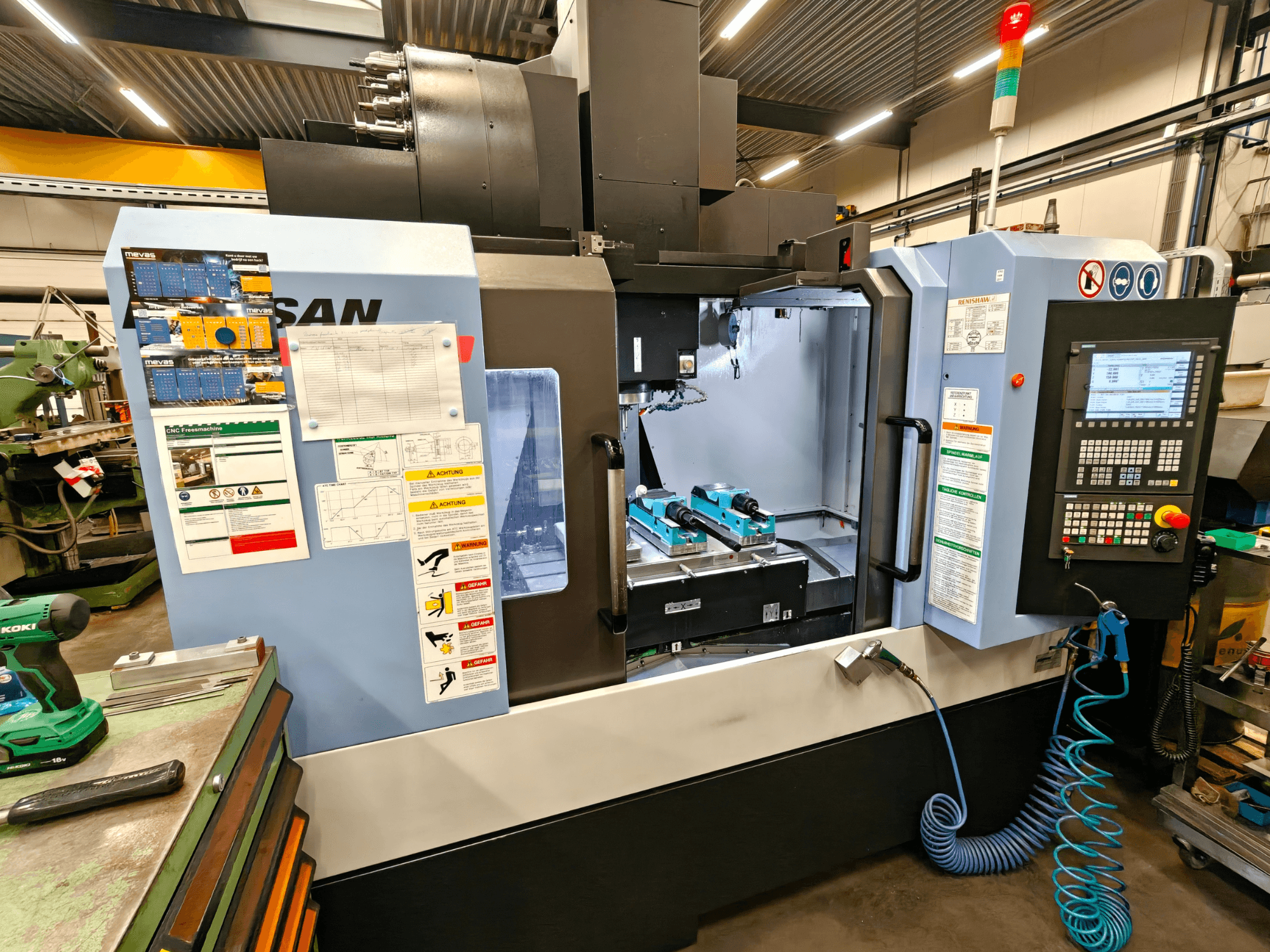 Vertikální obráběcí centrum DOOSAN DNM 400 II v dílně, s ovládacími prvky, držáky nástrojů a bezpečnostním značením, pohled zepředu.