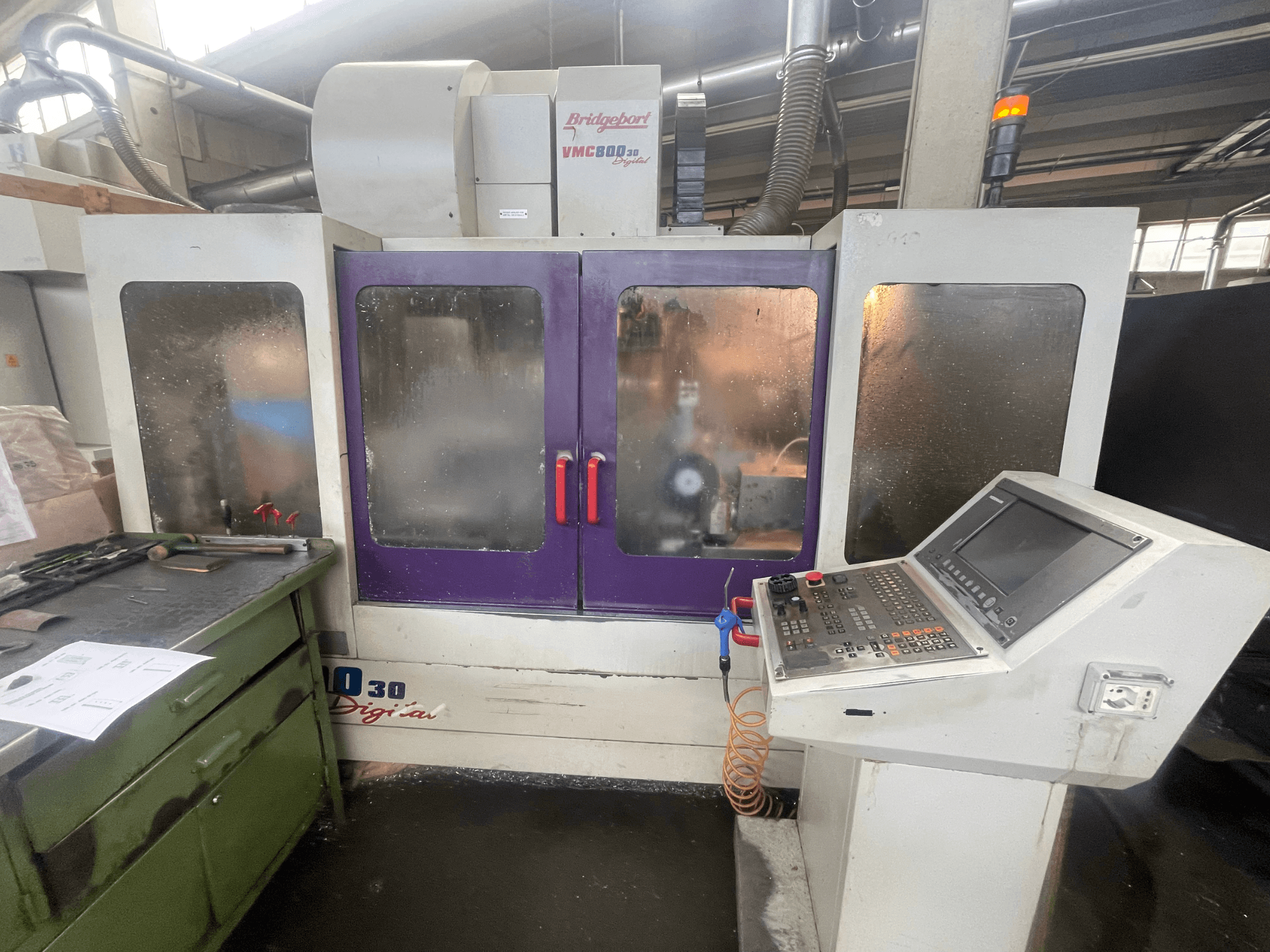 Vertikální obráběcí centrum Bridgeport VMC 800/30, pohled zepředu, na kterém je vidět ovládací panel a fialové dvířka, na přilehlé ploše leží nástroje.