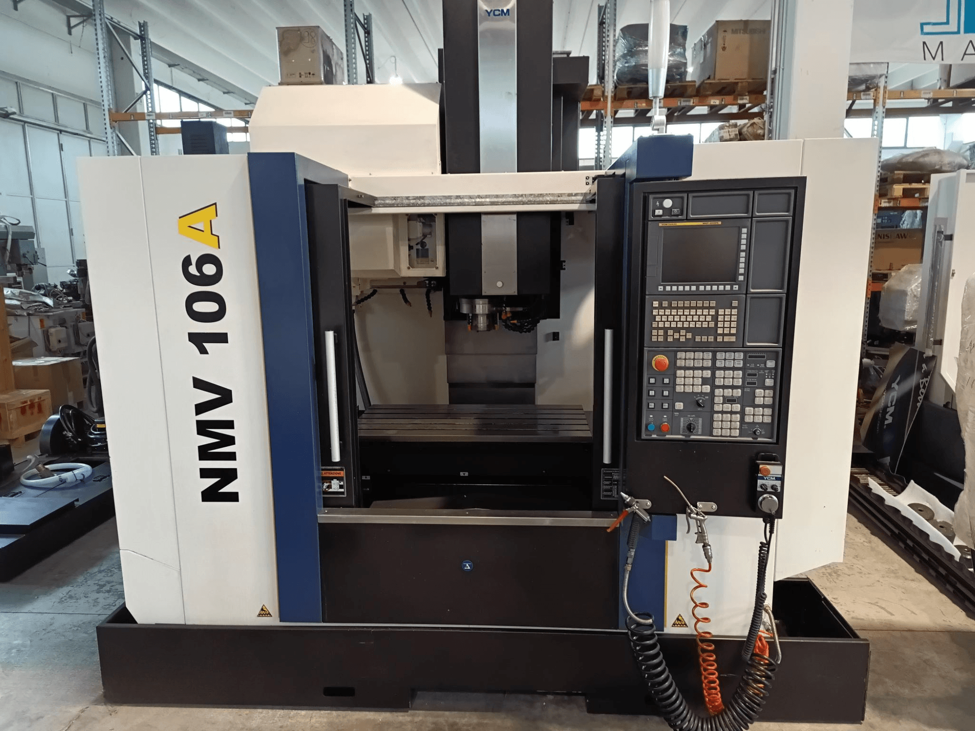 Obráběcí centrum YCM NMV 106A, pohled zepředu, ovládací panel s tlačítky a hadicemi chladicí kapaliny.