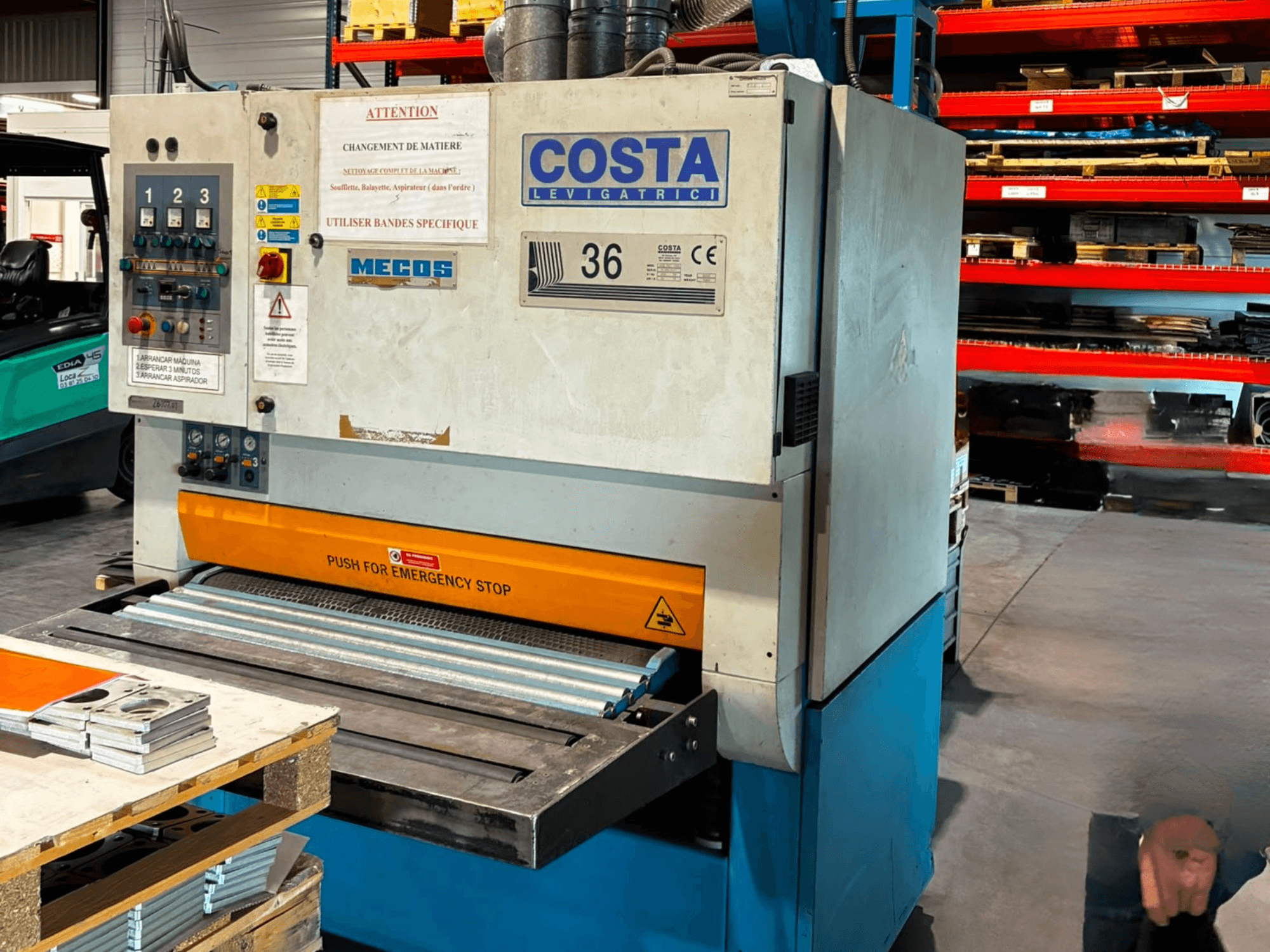 Odstraňovač otřepů Costa M36 CCS 1150 v bočním pohledu, s ovládacím panelem, nouzovým vypínačem a dopravníkovou plochou.